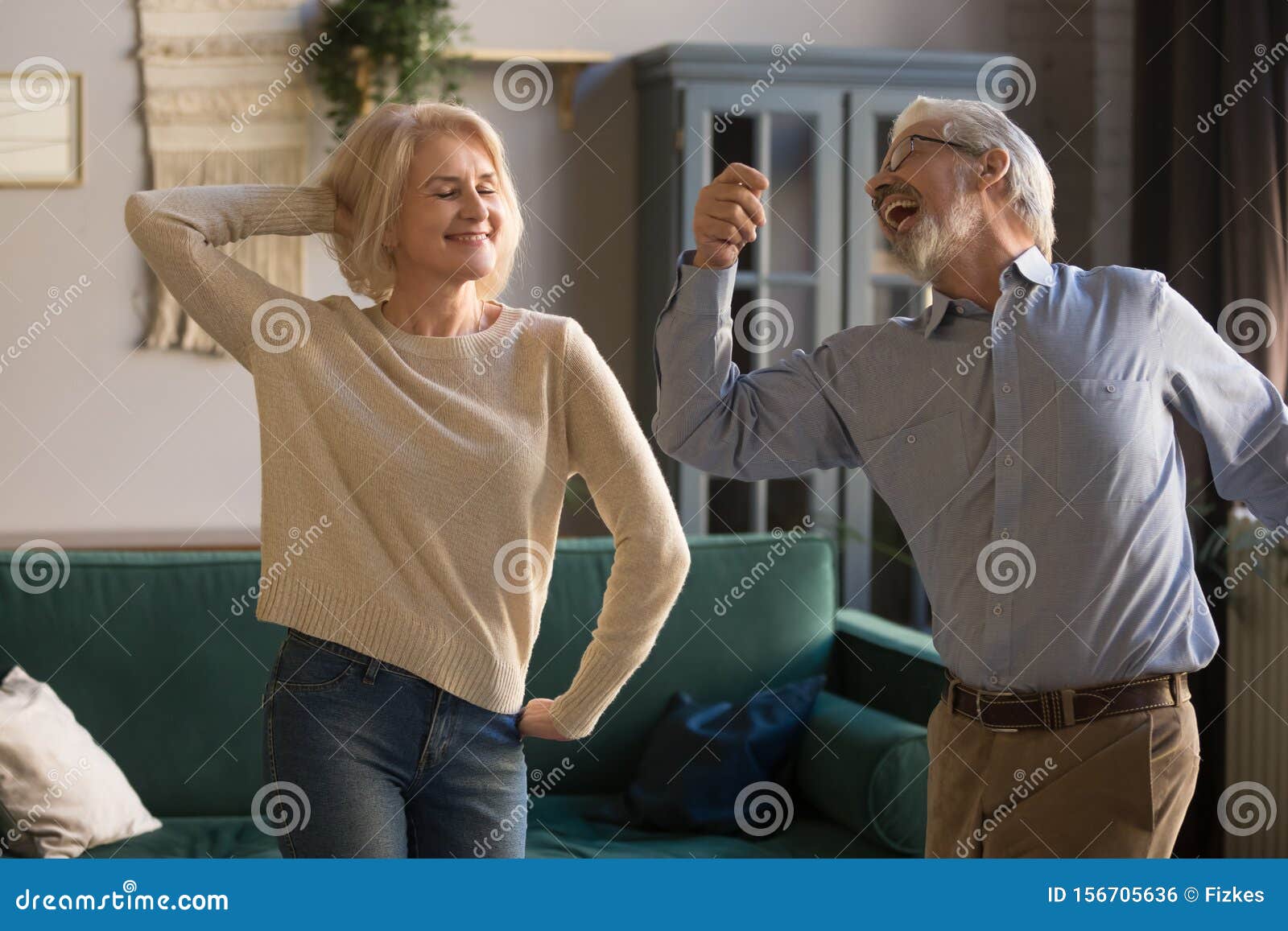 happy active retired elder couple dancing together in living room