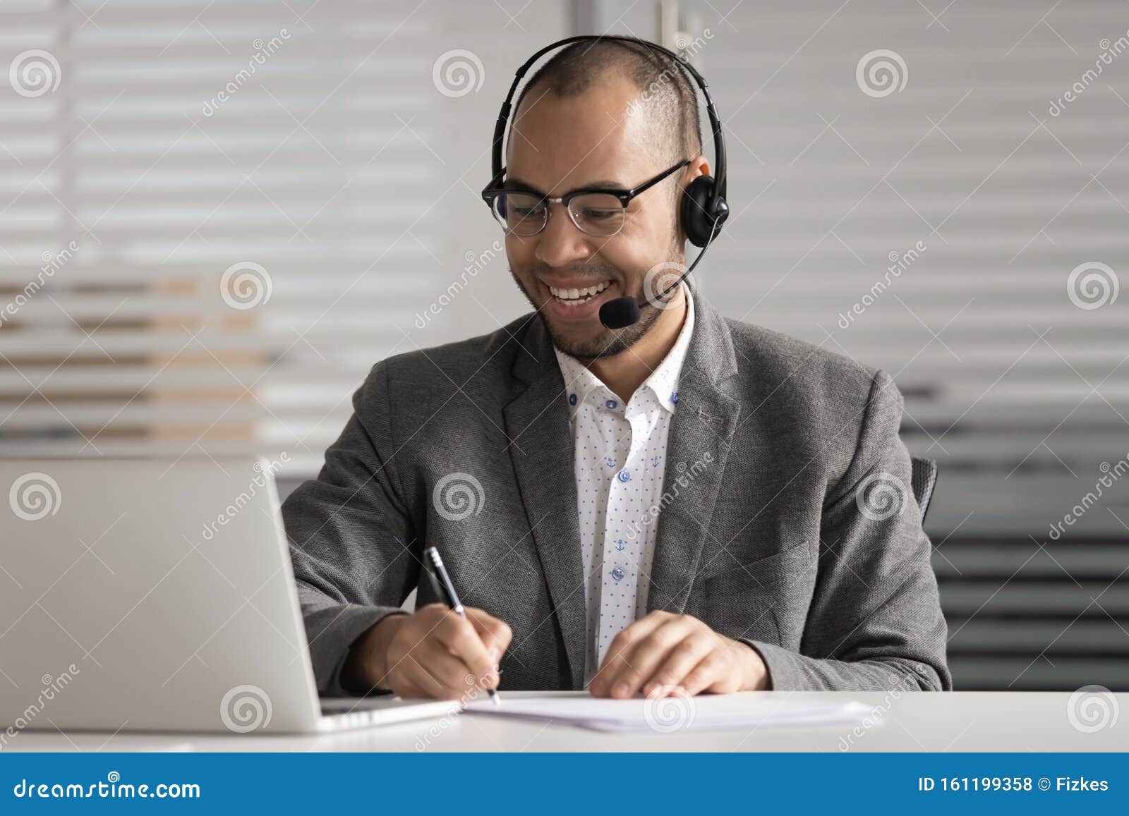 happy african american employee in headset making notes, using laptop
