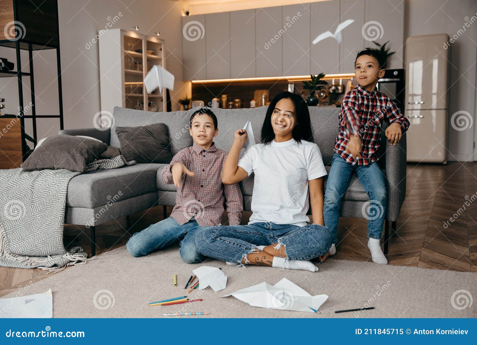 happy african american family, mother and two sons having fun time at home and fly paper airplanes