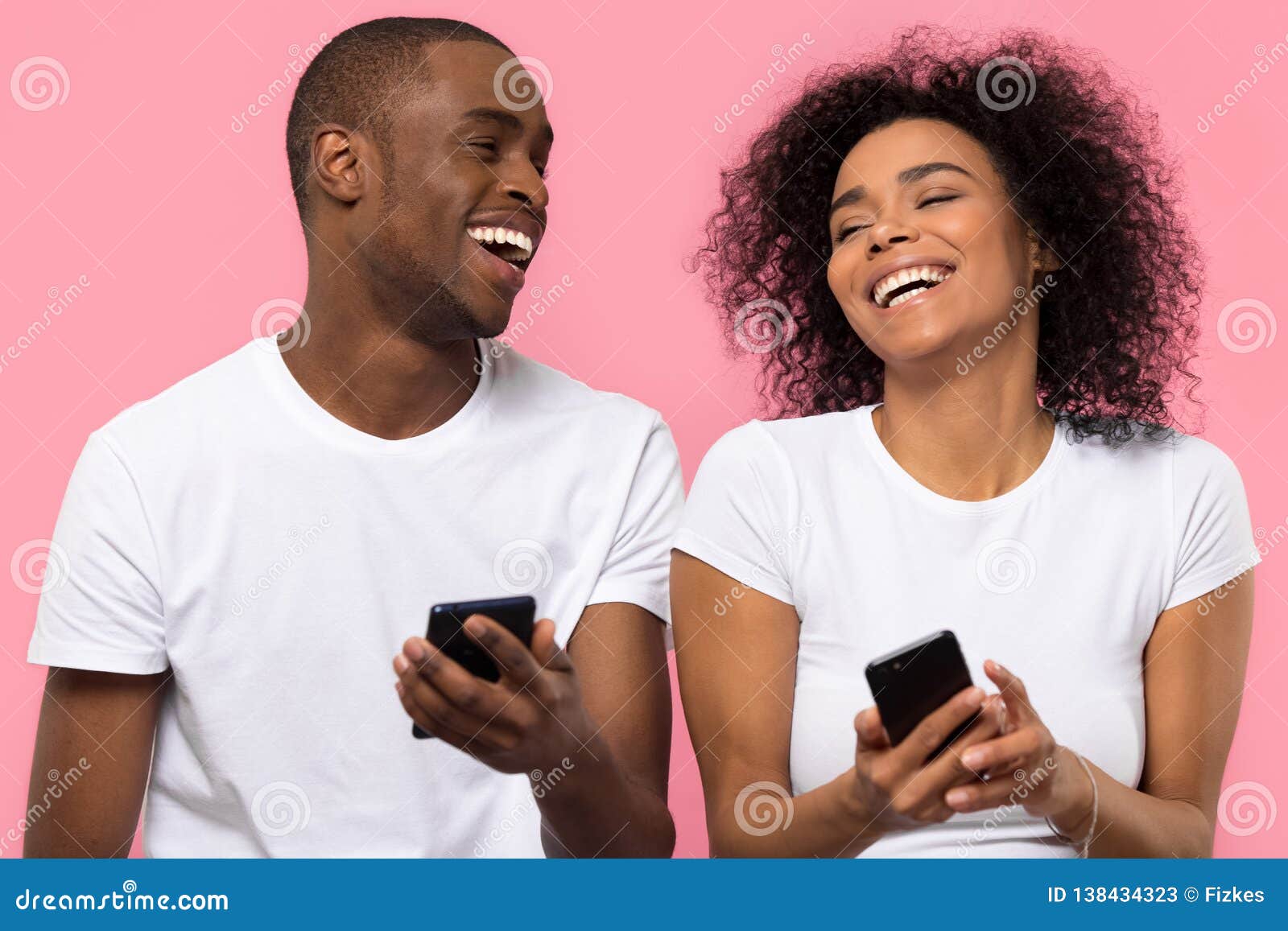 happy african couple laughing using smartphones  on pink background