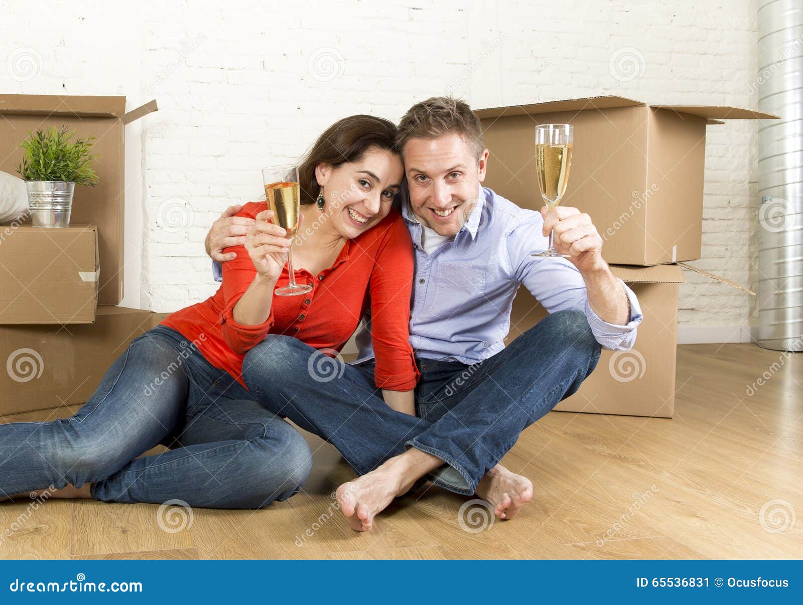 Happy American couple sitting on floor unpacking together celebrating with champagne toast moving in a new house. Young happy American couple sitting on floor unpacking boxes together celebrating with champagne toast moving in a new house or apartment in real estate and independent lifestyle concept