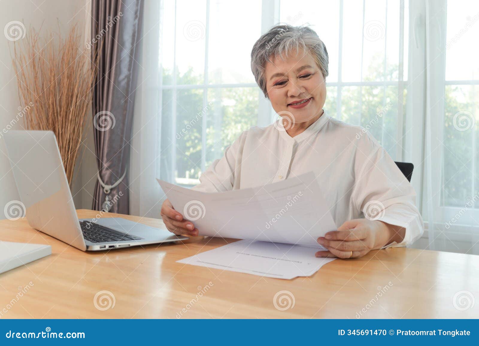 happy asian elderly woman reding document paper during sitting at desk at home. active mature senior woman working with document