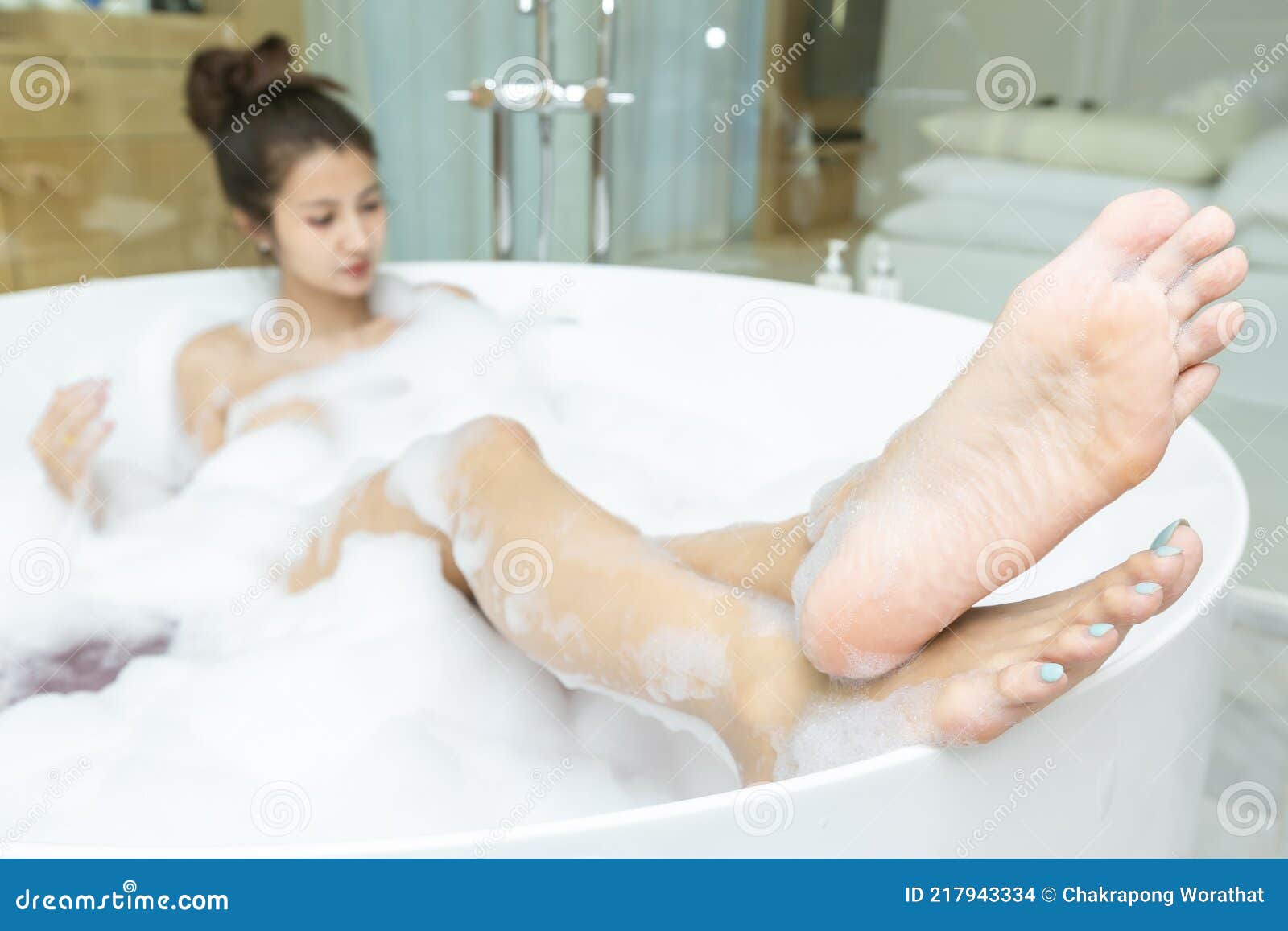 happy asian woman shaving her legs and having fun while lying in bathtub