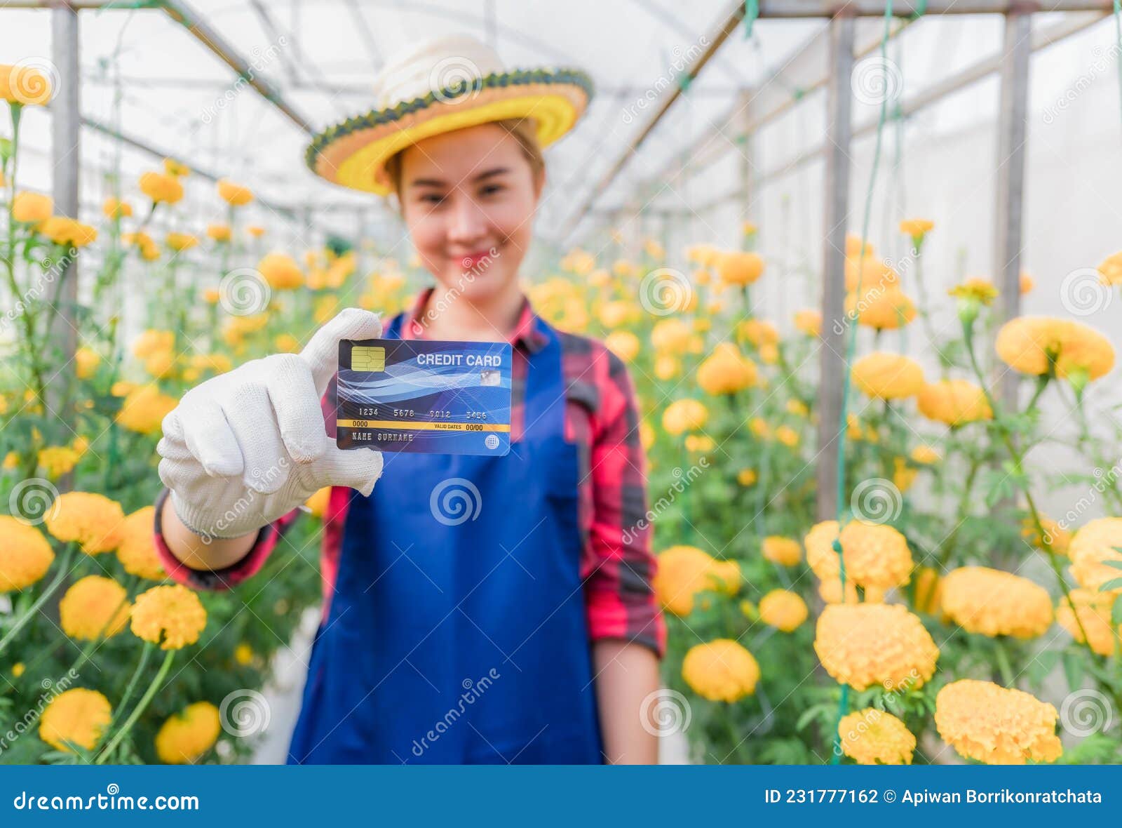 happy asian woman standing and holding credit card in yellow marigold garden