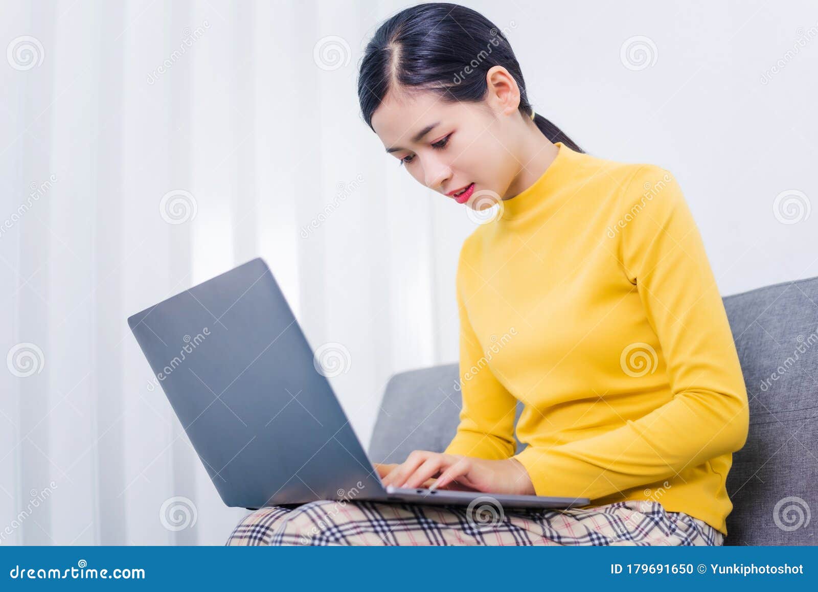 happy asian woman using laptop while sitting on sofa in living room, wfh work from home concept