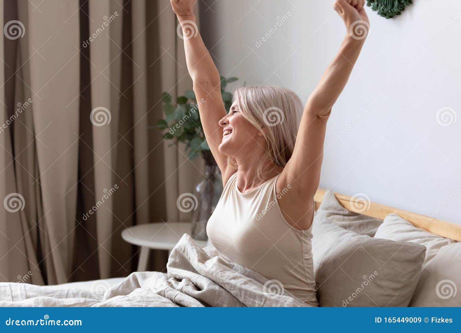 happy awakened aged woman stretching after night sleeping