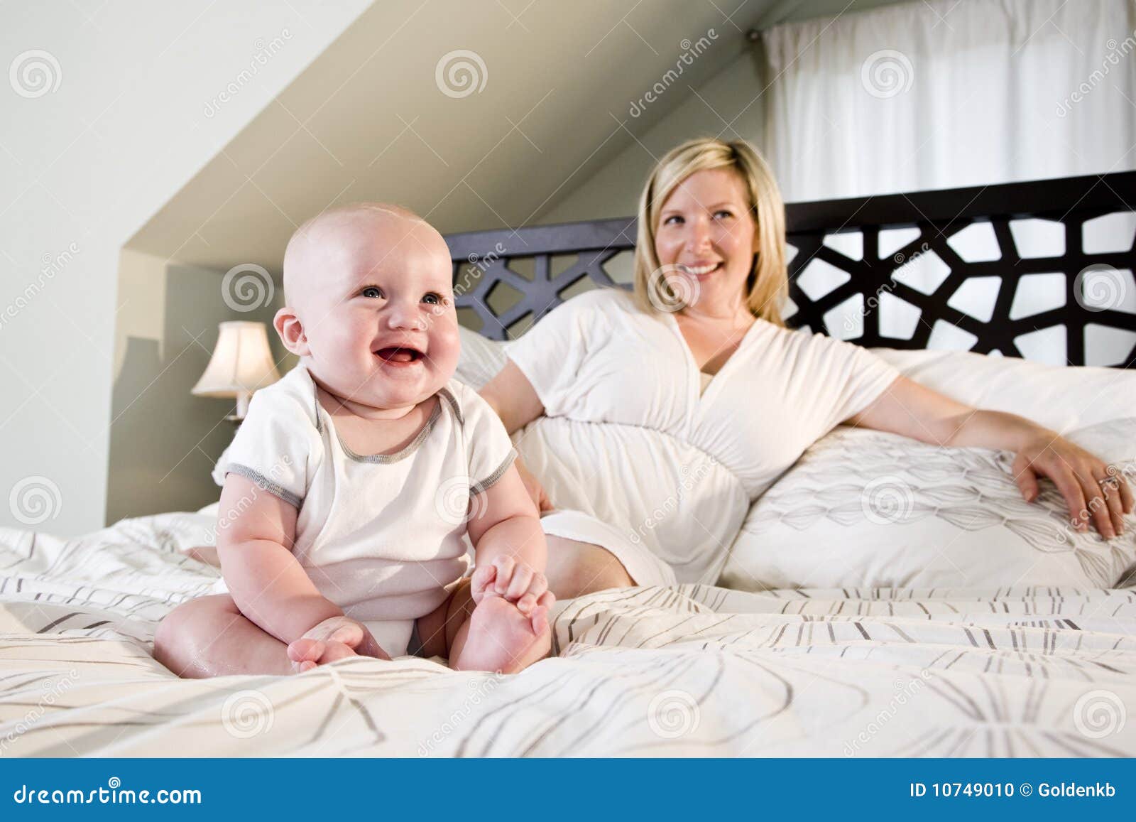 Happy Baby Sitting on Bed with Mother Stock Photo - Image of child ...