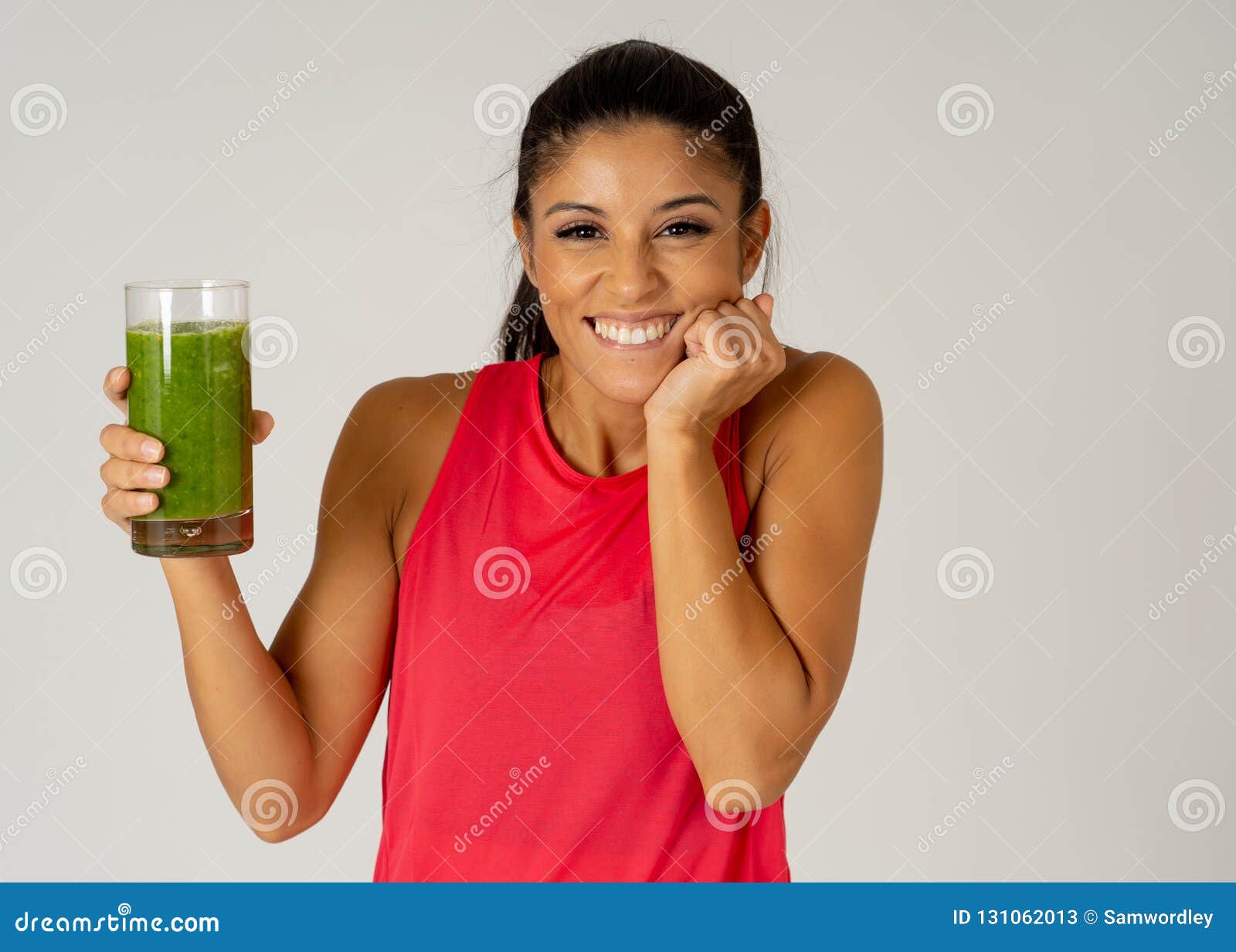 Happy beautiful fit sport woman smiling and drinking healthy fresh vegetable smoothie. Fitness woman happy smiling holding glass of green vegetable smoothie after fitness running workout isolated on gray background in Beauty Health Fitness Diet Nutrition and healthy Lifestyle concept.