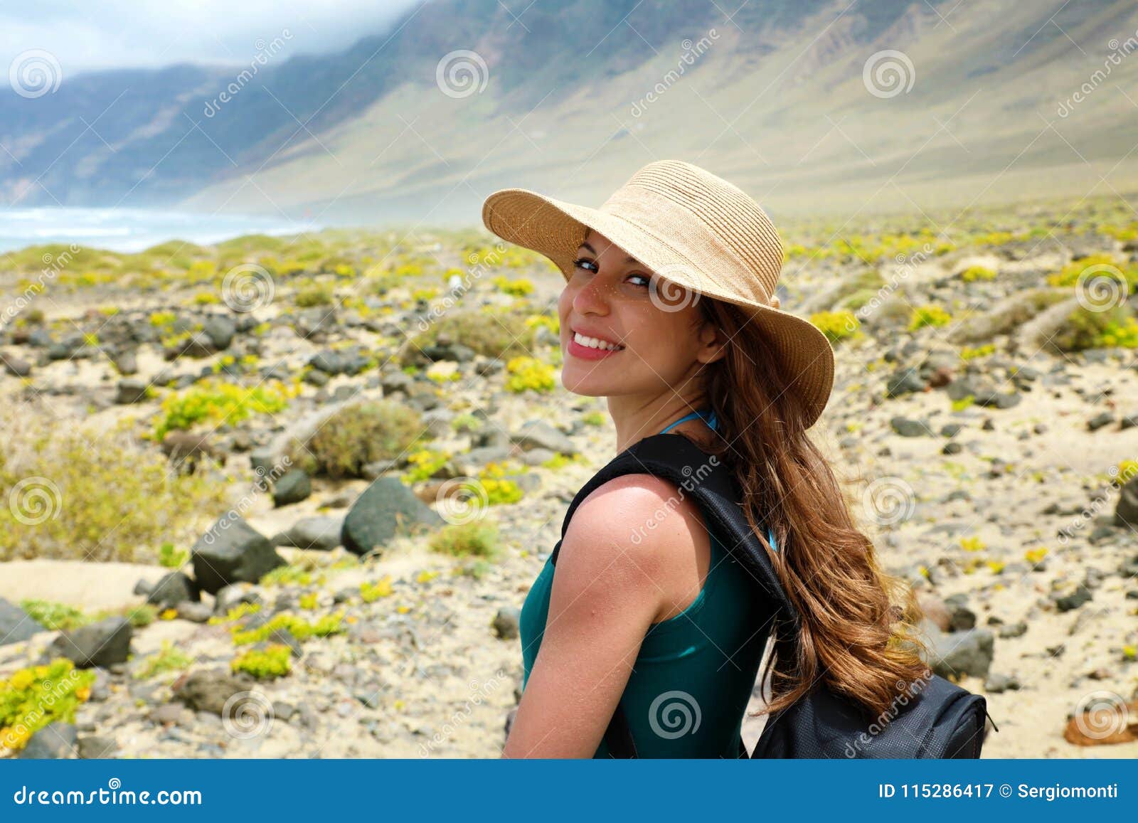 happy beautiful traveler girl with straw hat looking to the camera. young female backpacker exploring lanzarote, canary islands.