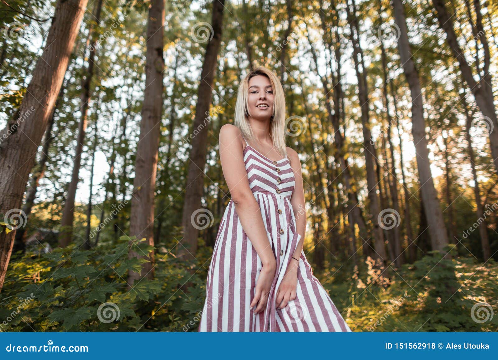 happy beautiful young blond woman with blue eyes with a sweet smile in a stylish pink striped dress walks in the park