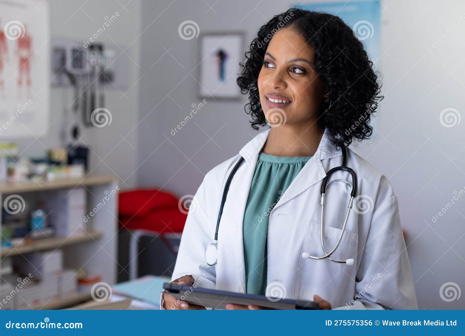 happy biracial female doctor wearing sthethoscope, using tablet at doctor's office
