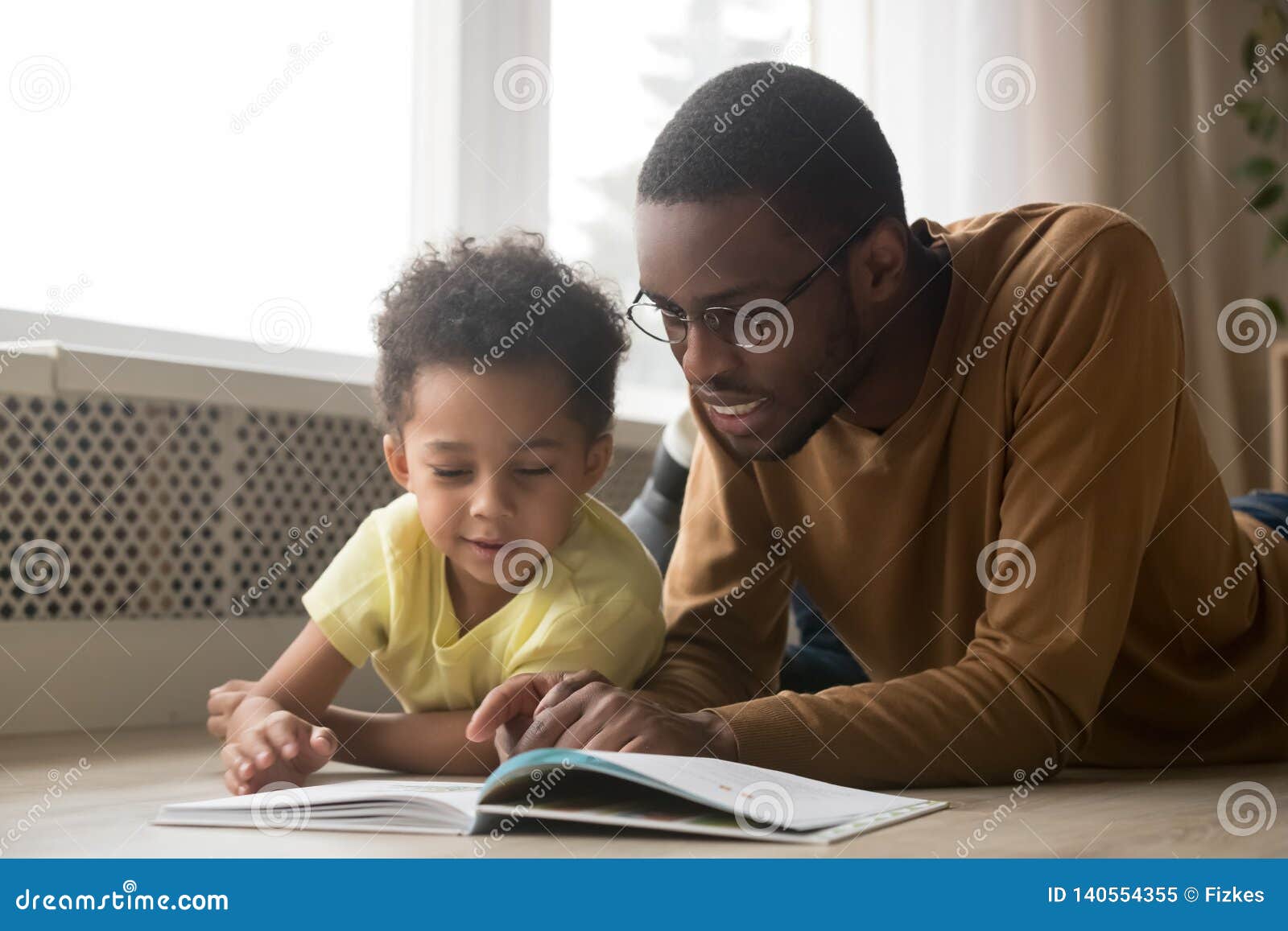 happy black father and toddler son reading book at home