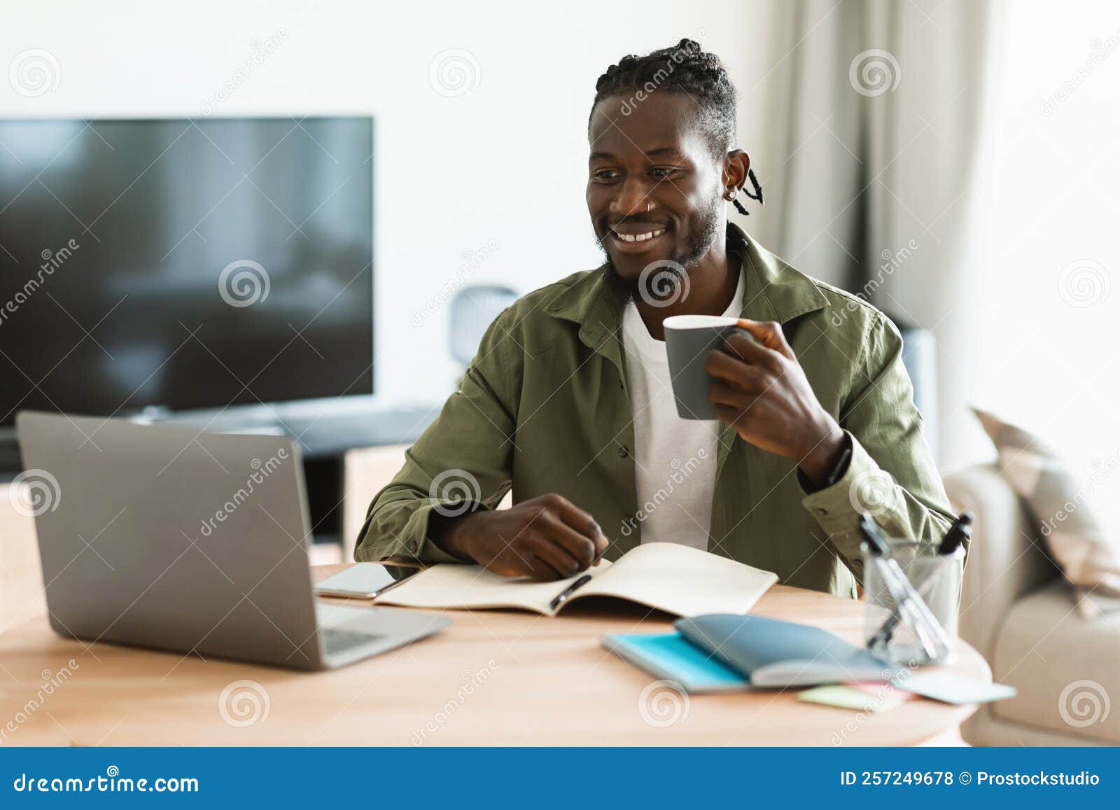 Happy Black Man Drinking Cup of Tea at Workplace while Working on