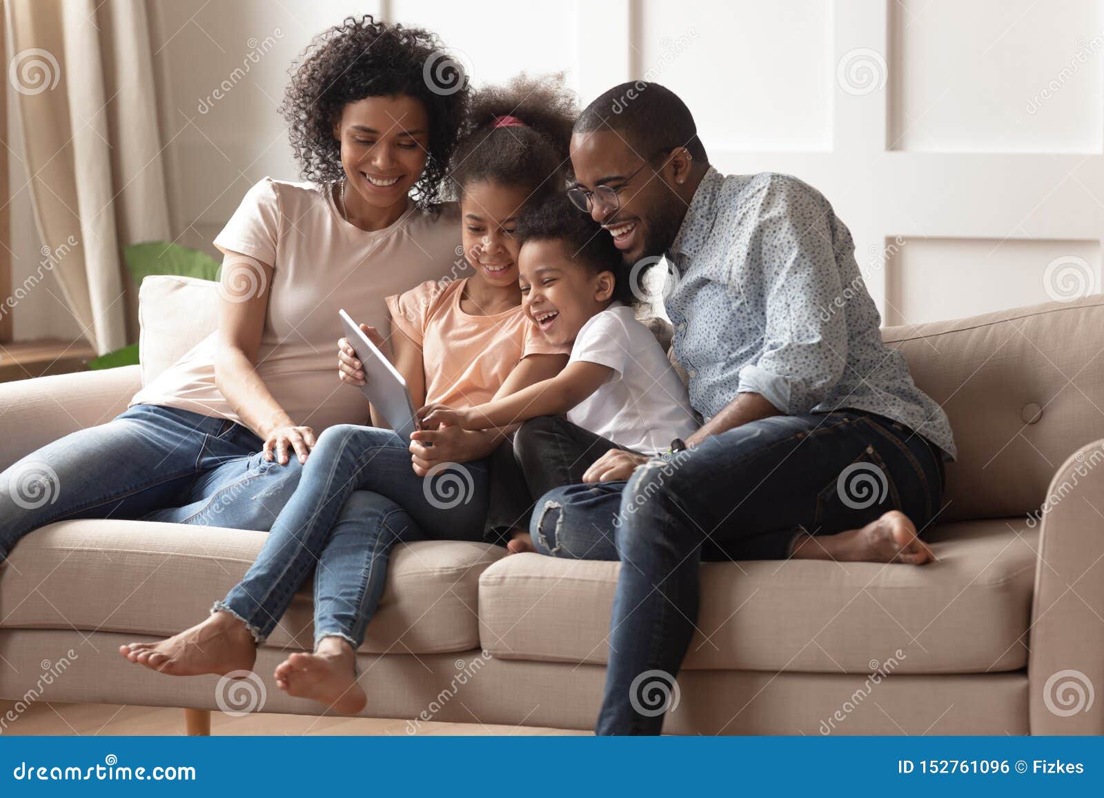 happy black parents and children using digital tablet on sofa