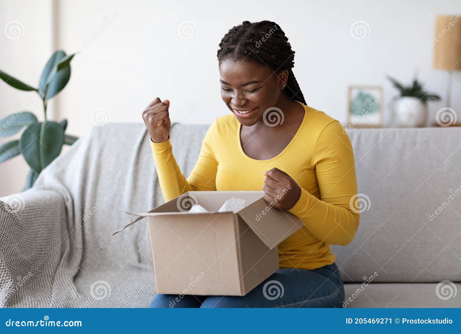 happy black woman unboxing parcel at home, emotionally reacting to successful shopping