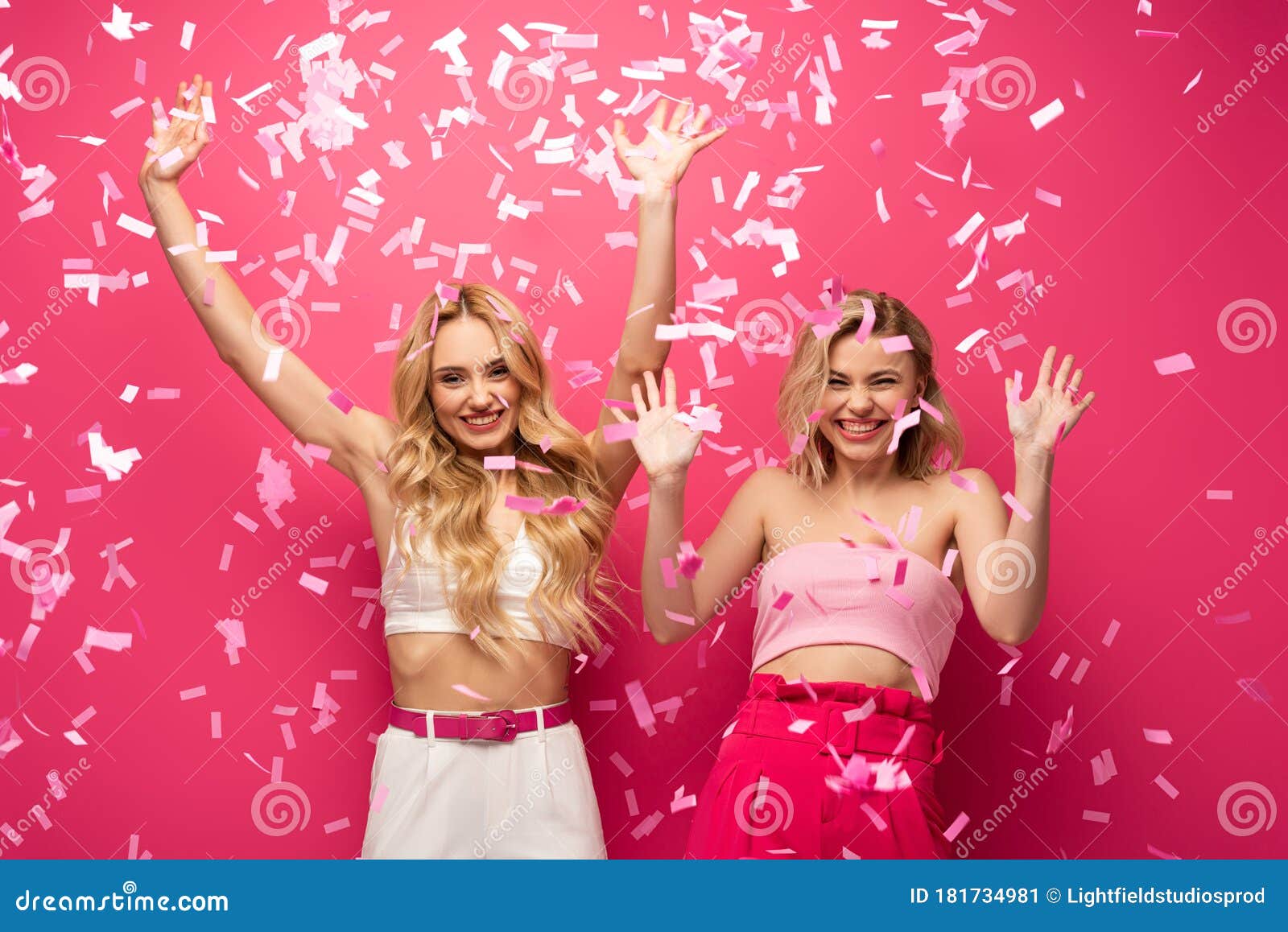 Blonde Friends Looking at Camera Under Falling Confetti on Pink