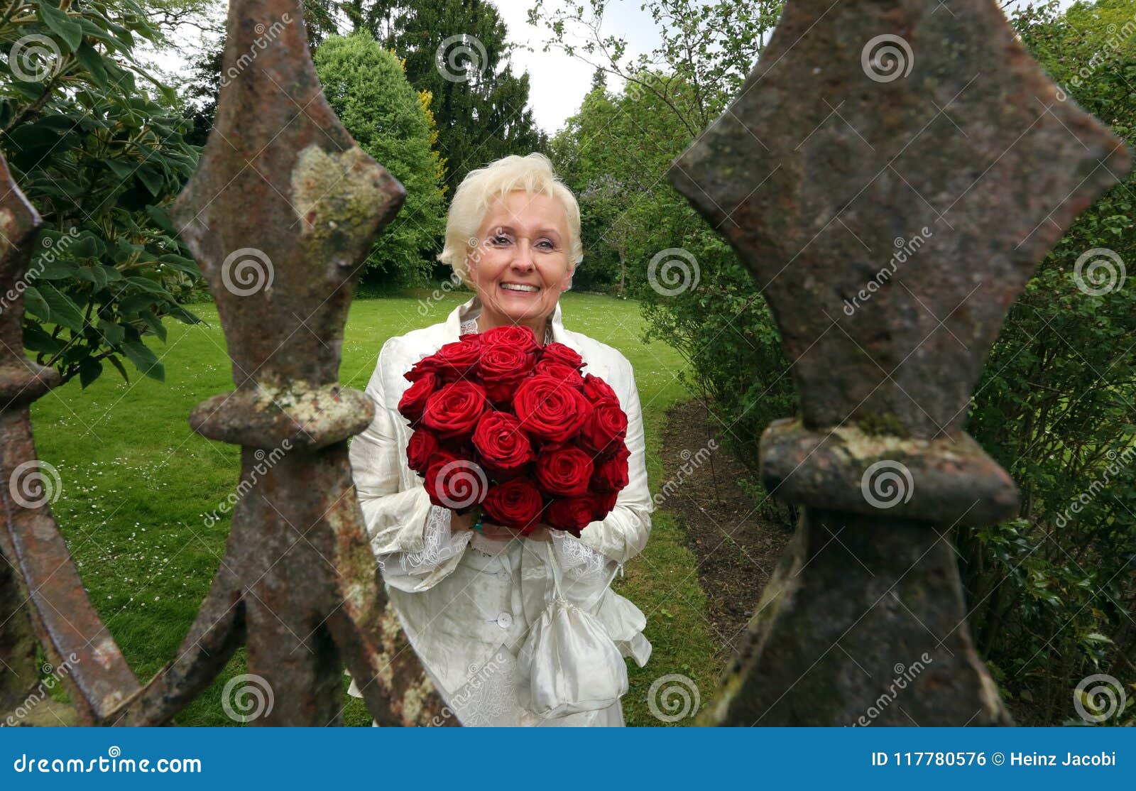 happy bride with red roses photographed through the old castle fence