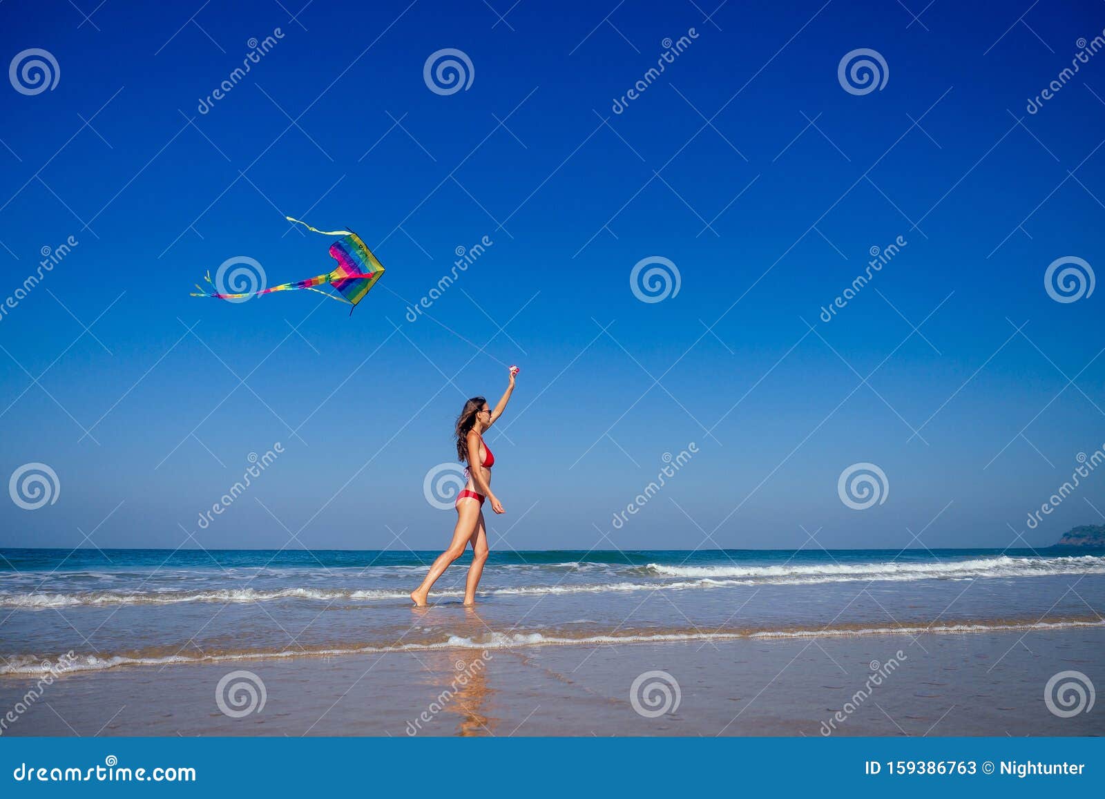 happy brunette girl in a bathing suit and short pink playing with flying kite on tropical beach copyspase hills and