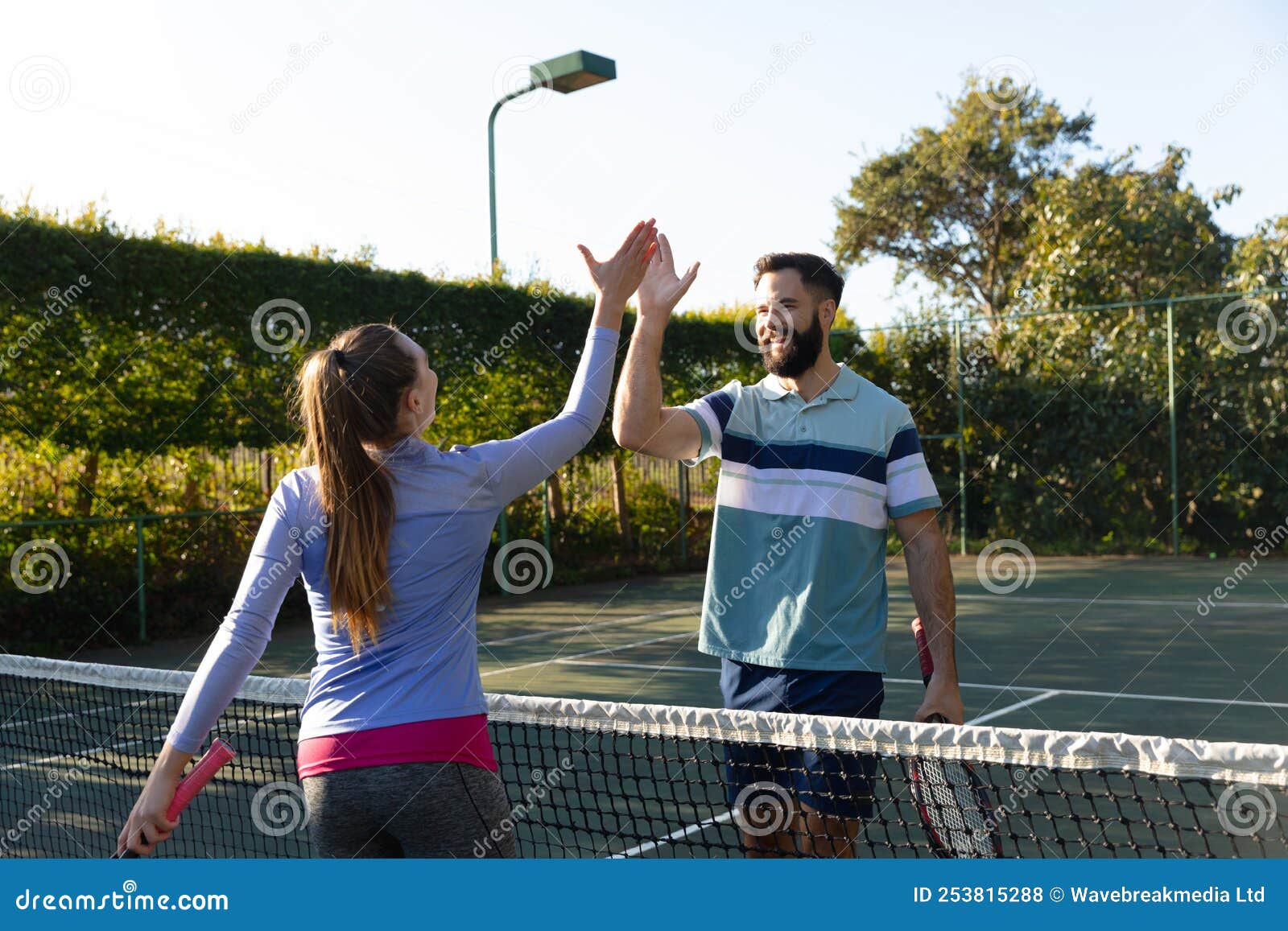 Happy caucasian couple playing tennis shaking hands over the net on