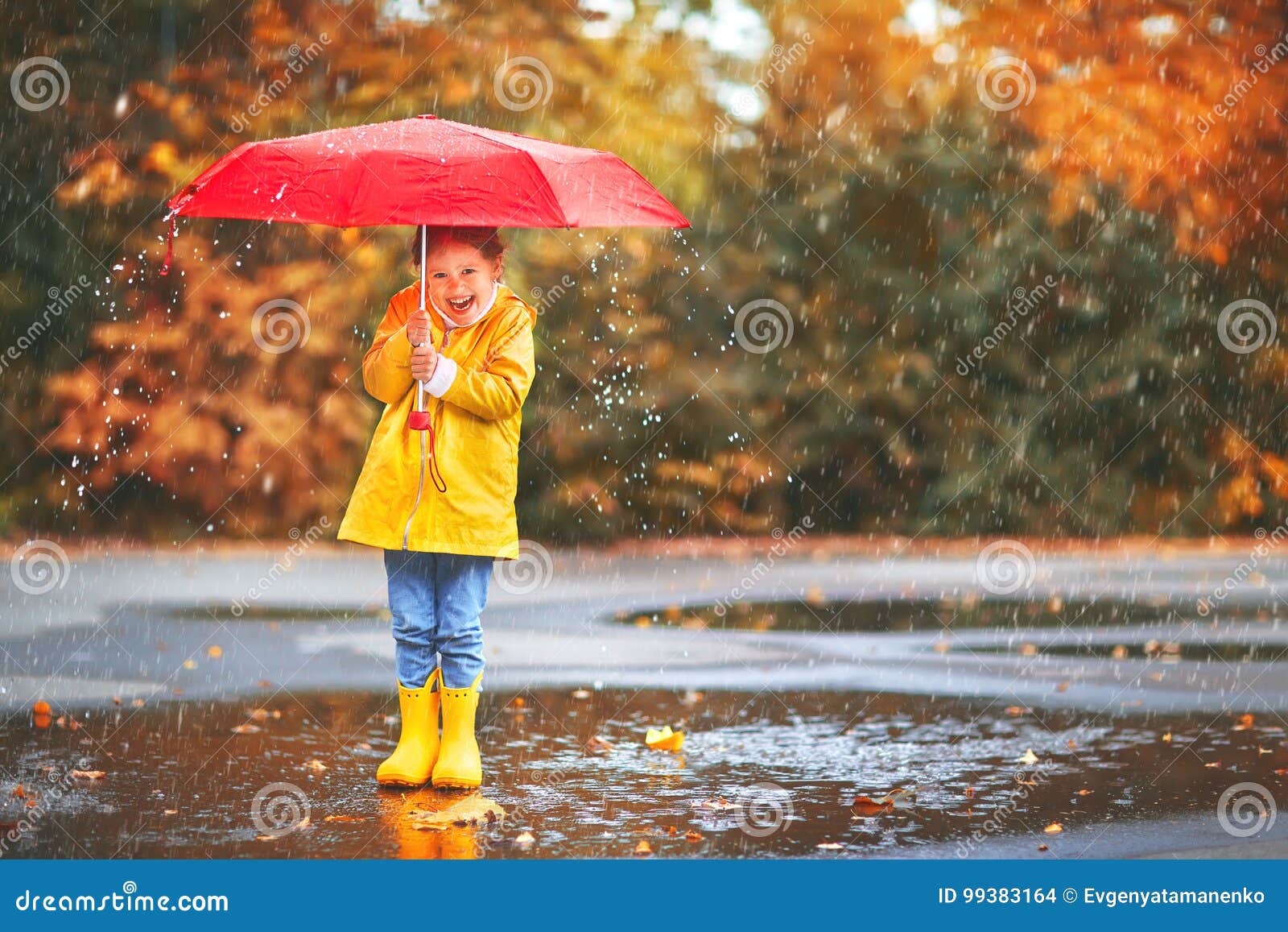 happy child girl with an umbrella and rubber boots in puddle on