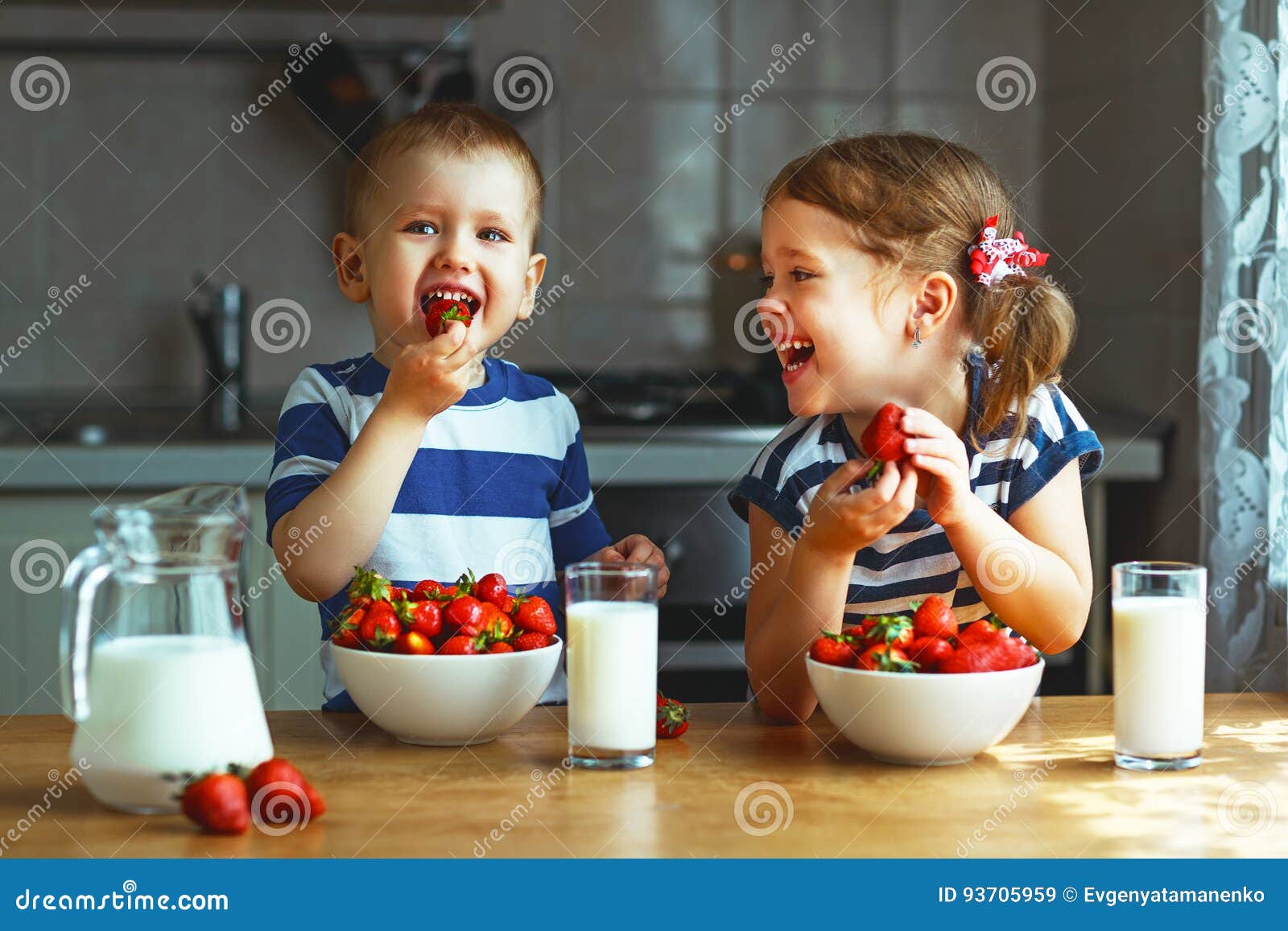 happy children brother and sister eating strawberries with milk