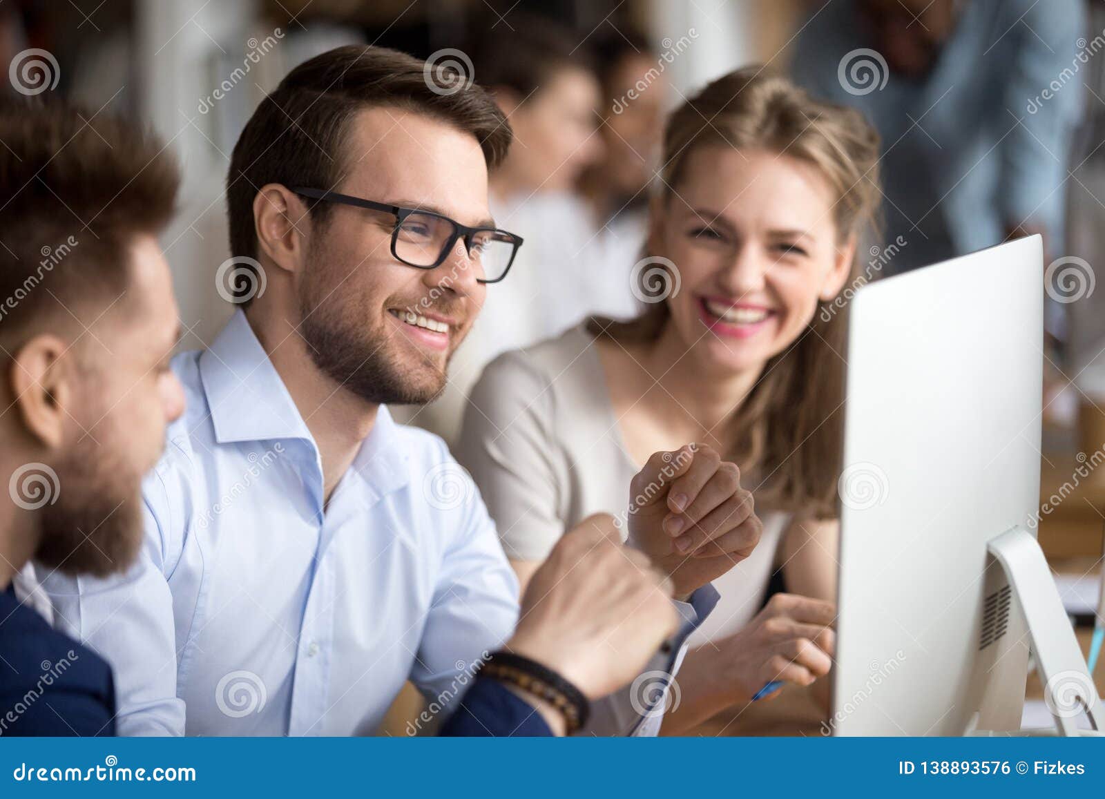 happy colleagues looking at computer screen talking laughing working together