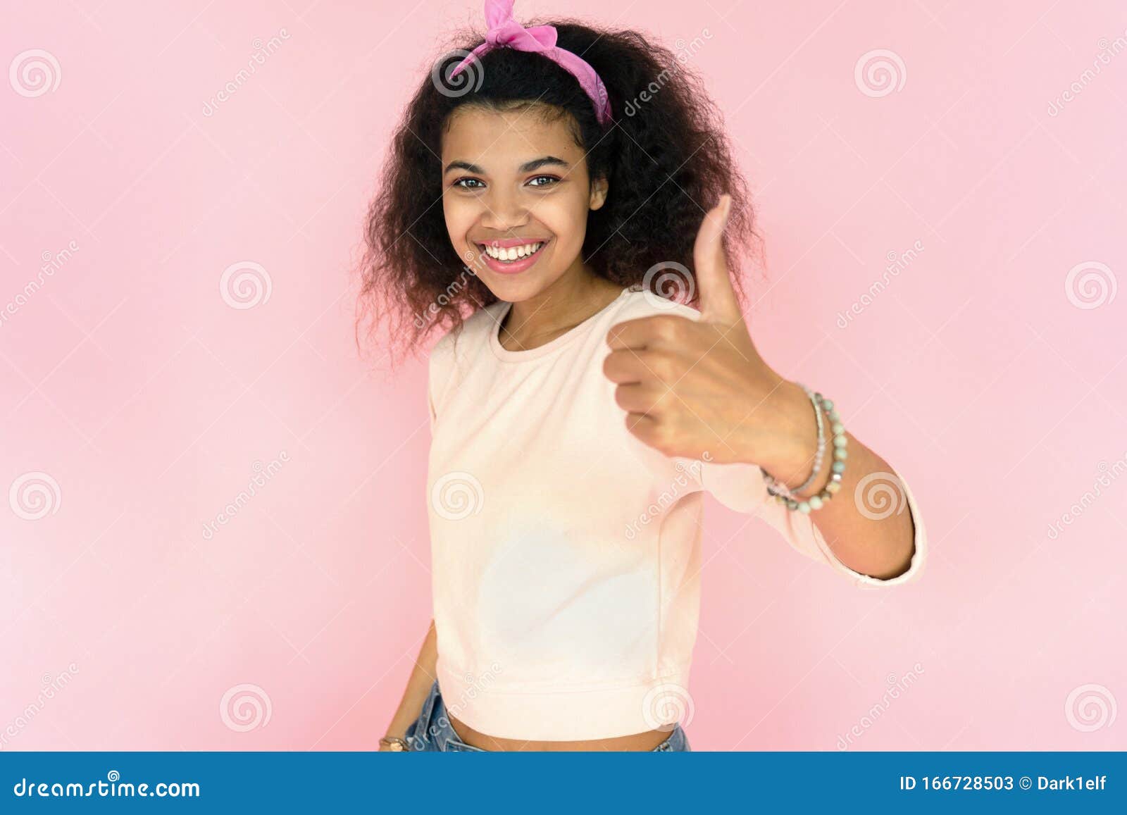 happy african girl look at camera show thumbs up on pink studio background