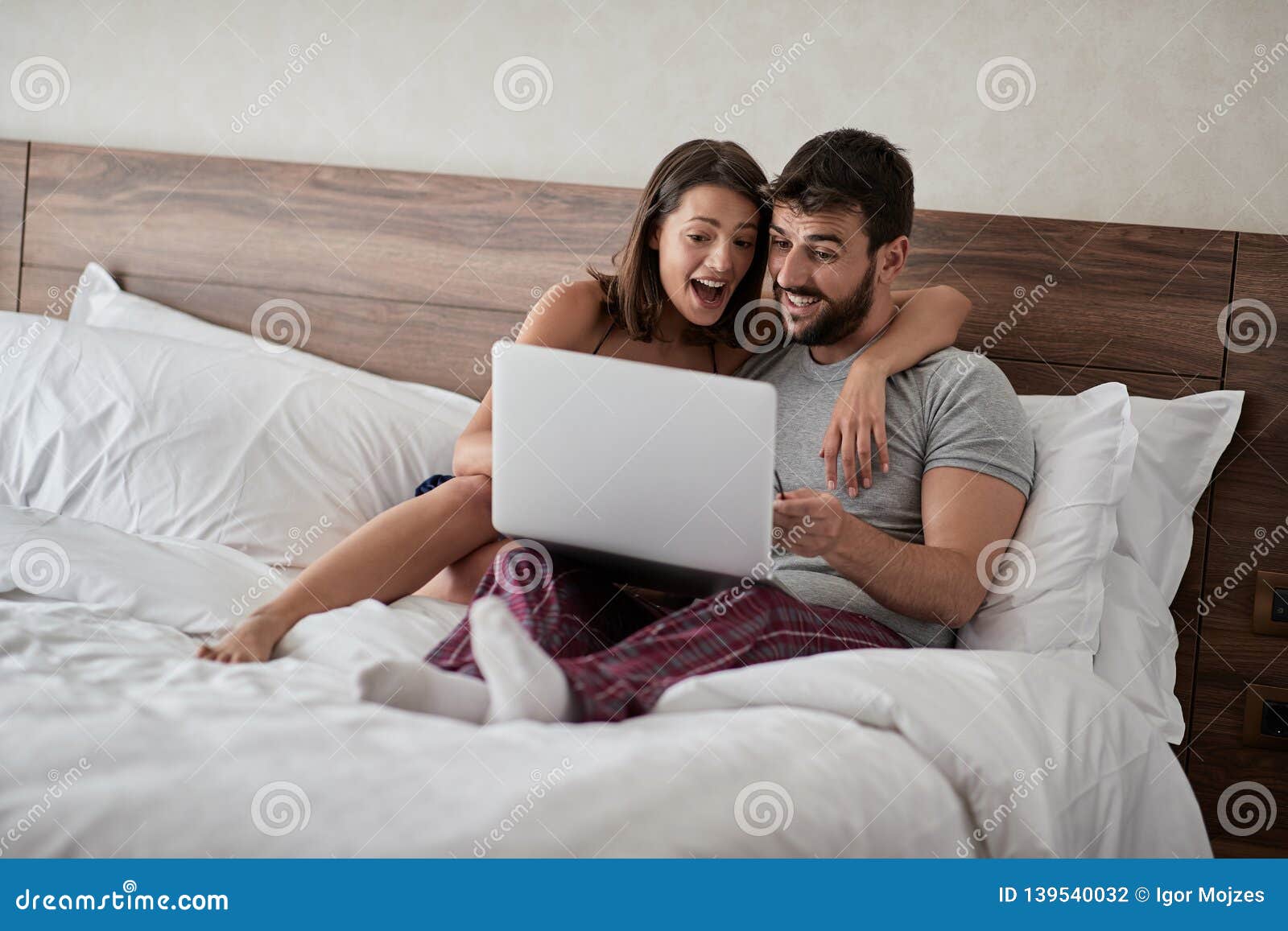 Happy Couple Lying on a Bed with Computer - Beautiful Married Couple Watching Sex Video on Laptop Laughing Together - People, Stock Photo image