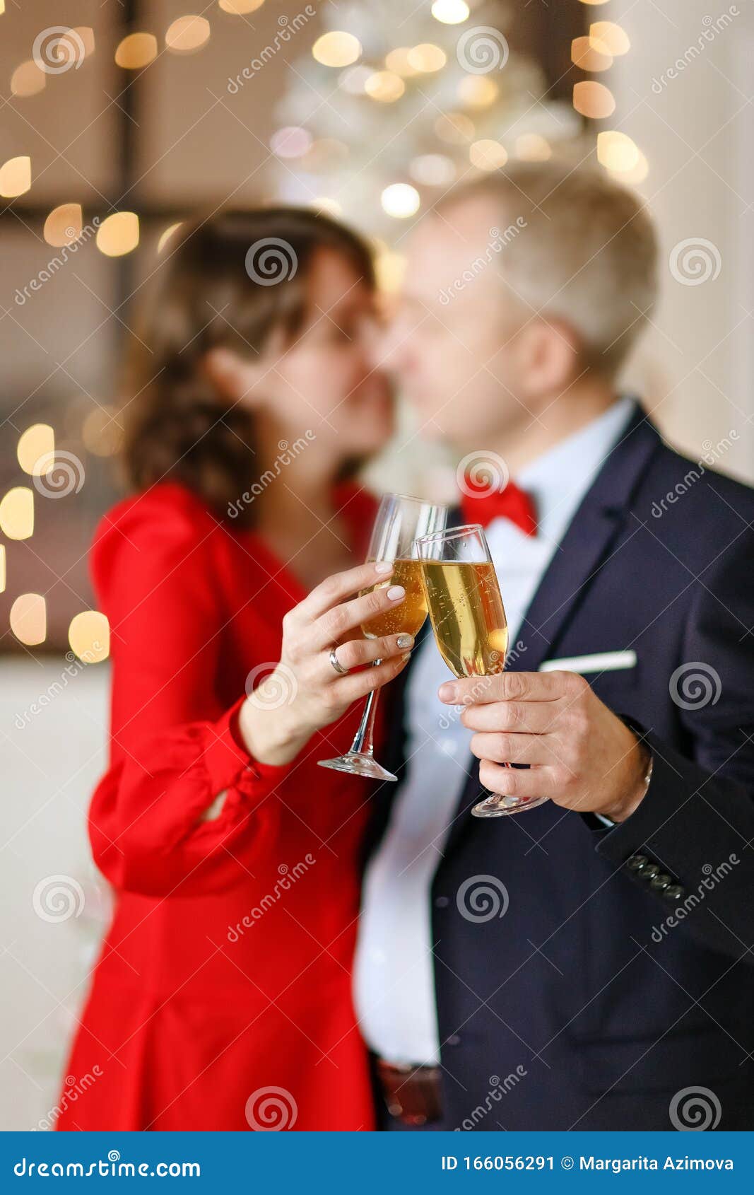 Happy couple of people with two glasses of champagne on the background of Christmas lights in a bright studio. Object out of focus. Close-up