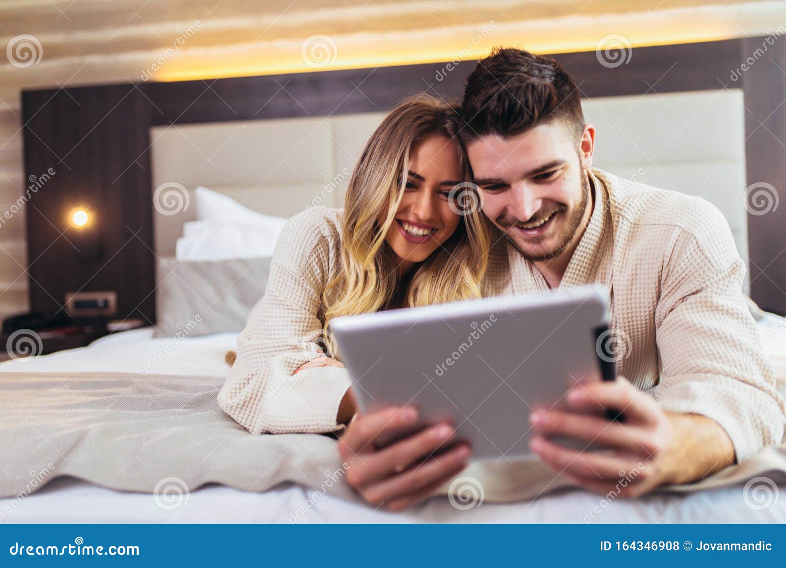 Couple Using Digital Tablet While Lying Together In Bed In Hotel Roo