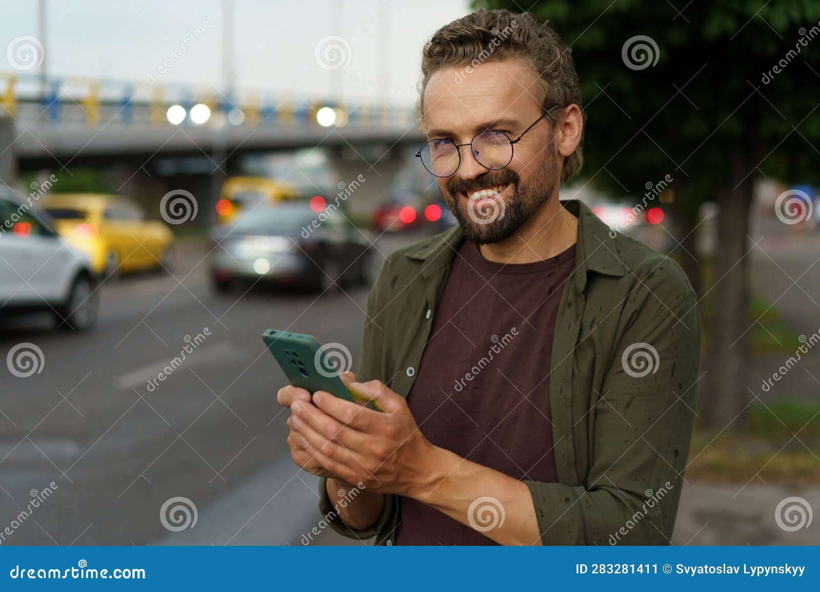 happy customer making order for taxi cab. with smile on face, man uses phone to book ride while dusk sets in and street
