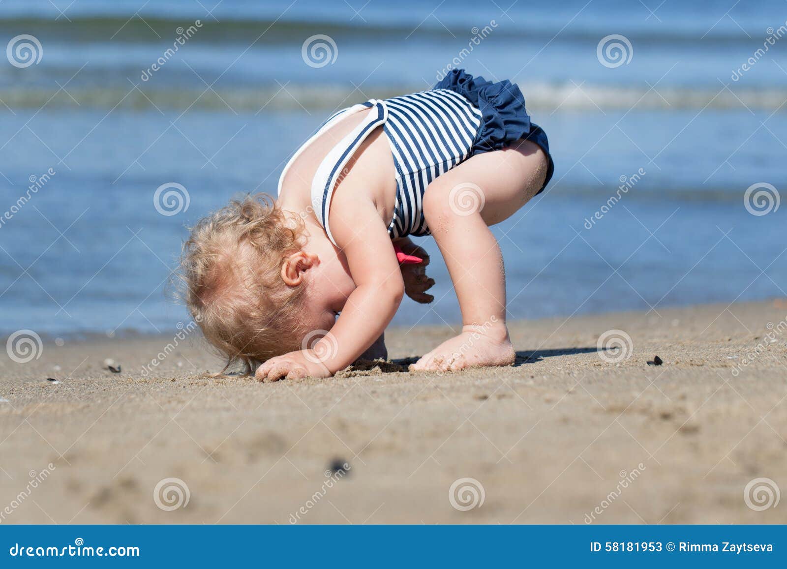 Happy cute girl in swimsuit playing with sand on beach. Happy pretty baby girl in swimsuit playing with sand on beach