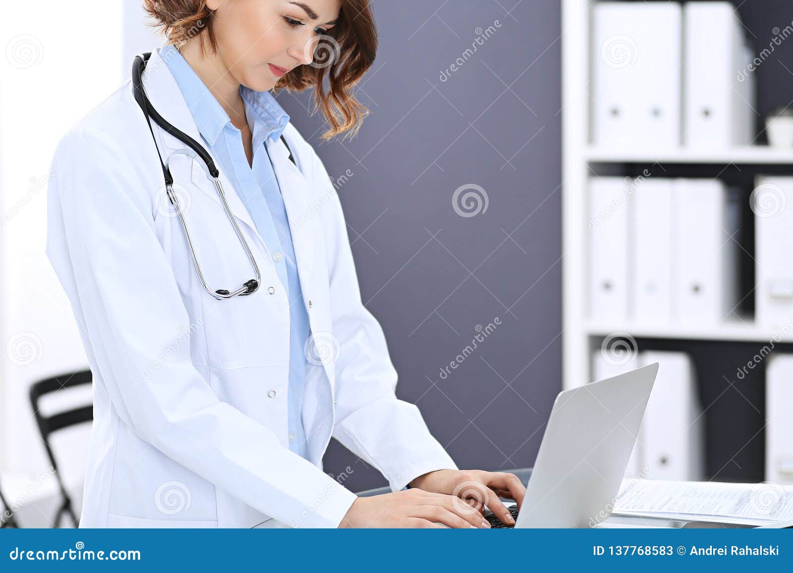 happy doctor woman at work. portrait of female physician using laptop computer while standing near reception desk at
