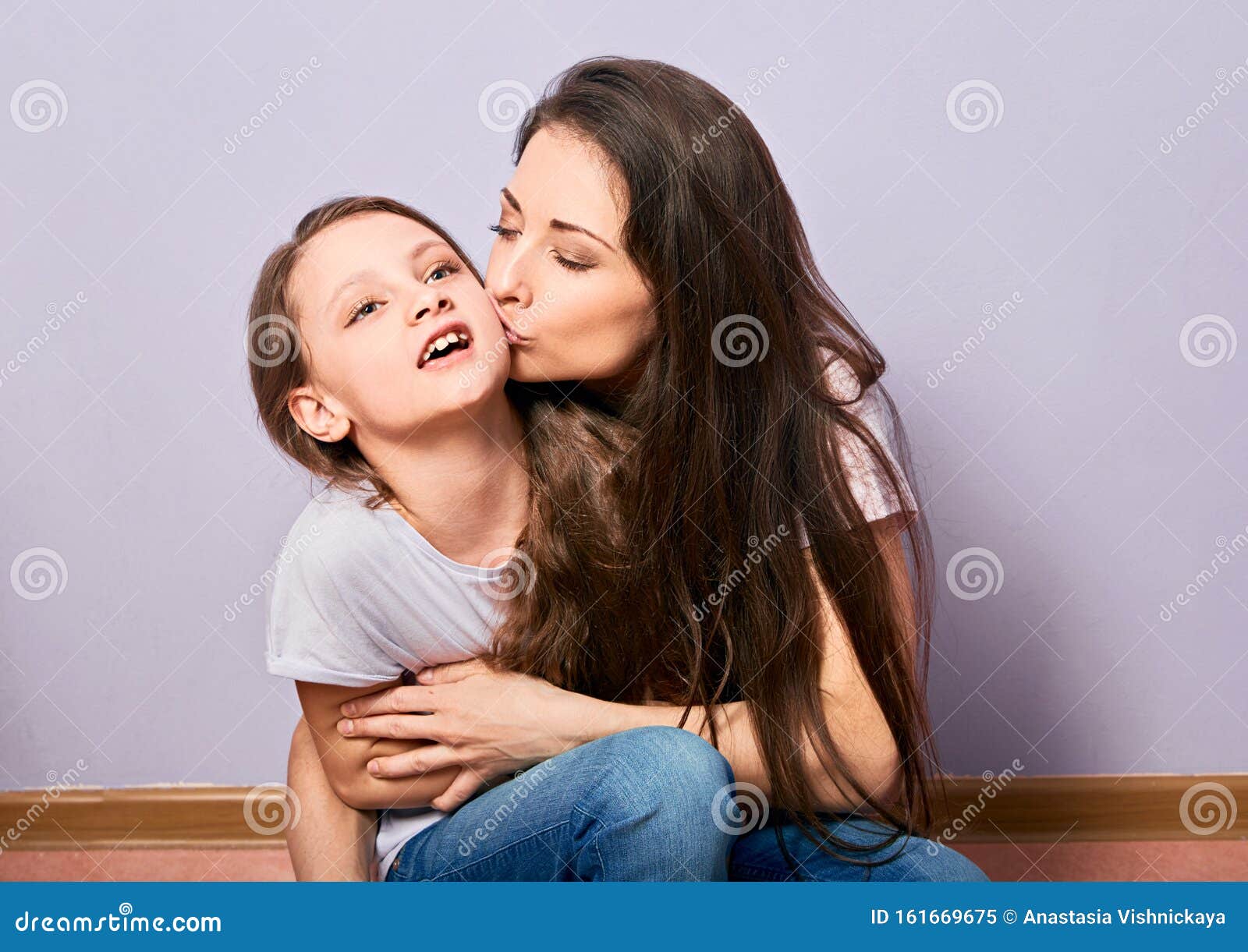 Happy Excited Mother Cuddling And Kissing Her Daughter On Purple Background With Empty Copy 