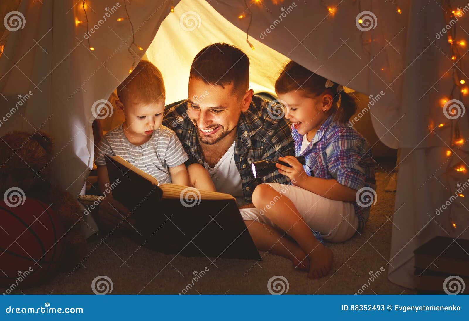 happy family father and children reading a book in tent at hom