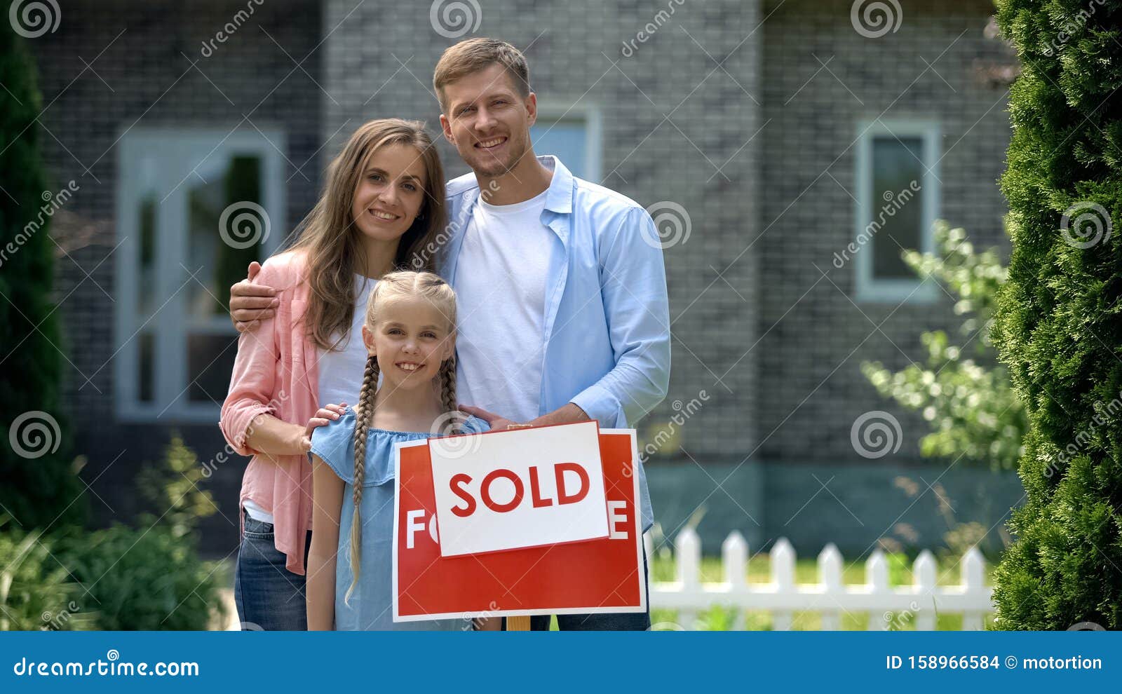 happy family holding sold sign, standing against new bought house, thumbs up