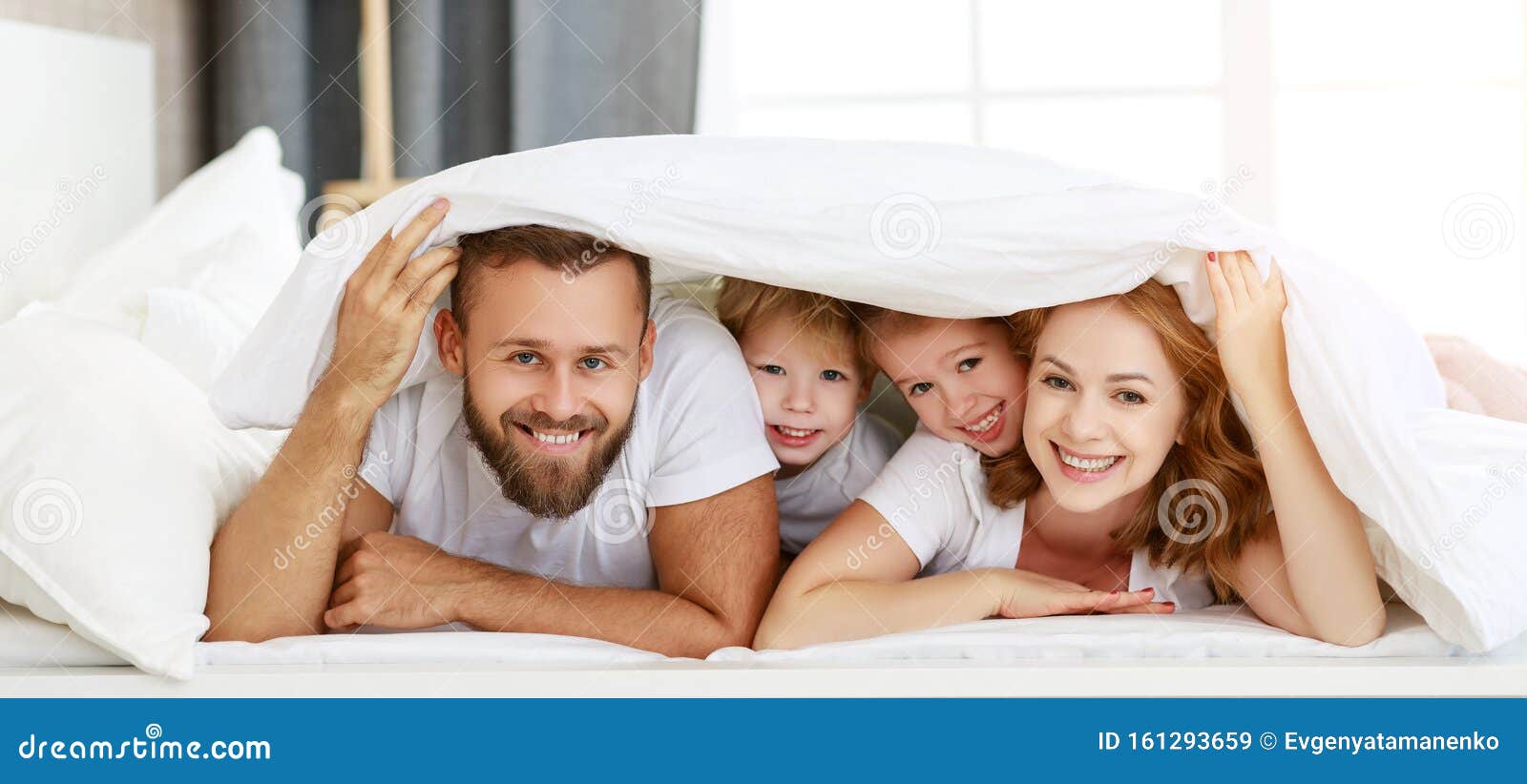 happy family mother, father and children laughing, playing and smiling in bed   at home