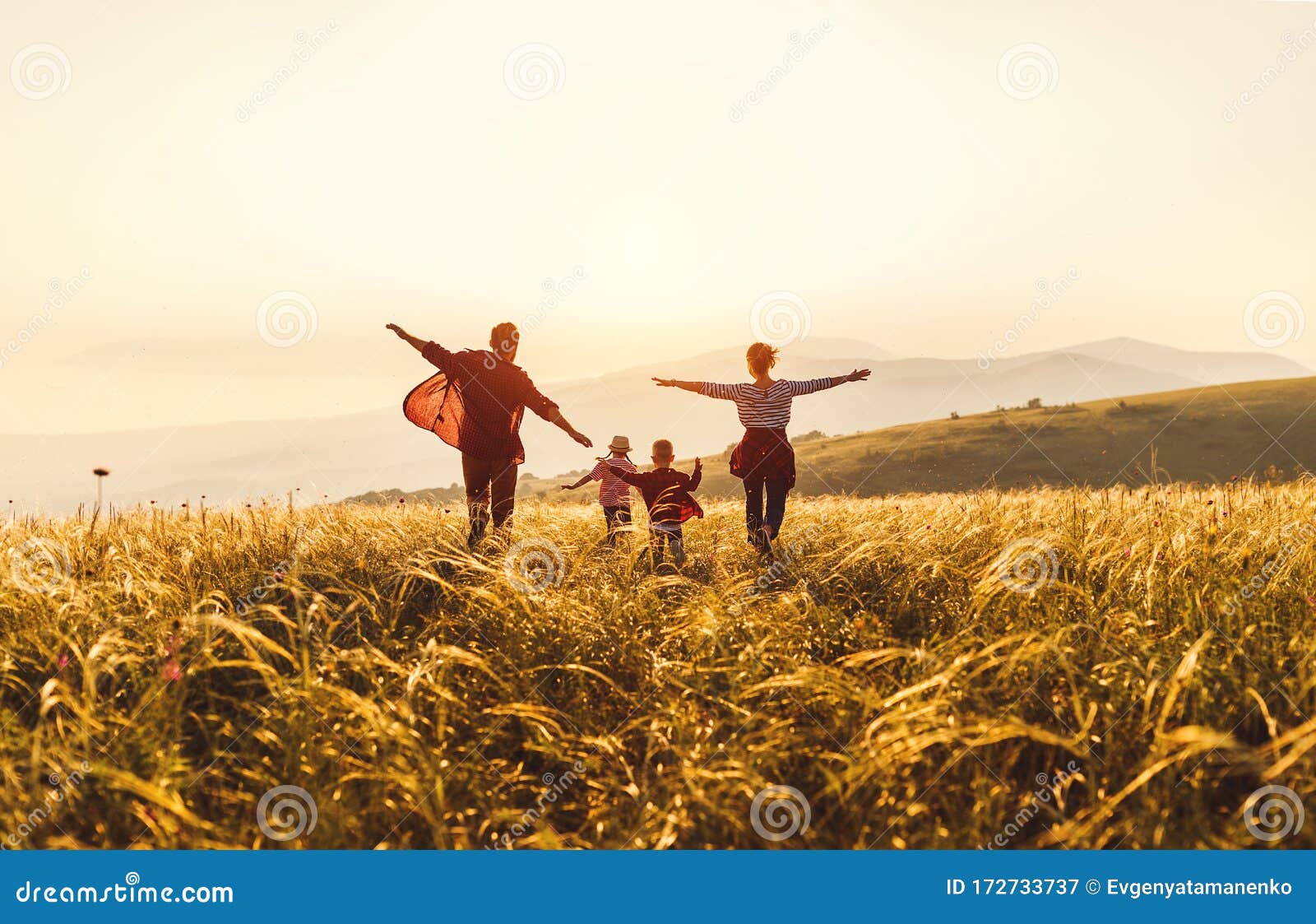 happy family: mother, father, children son and daughter runing and jumping on sunset