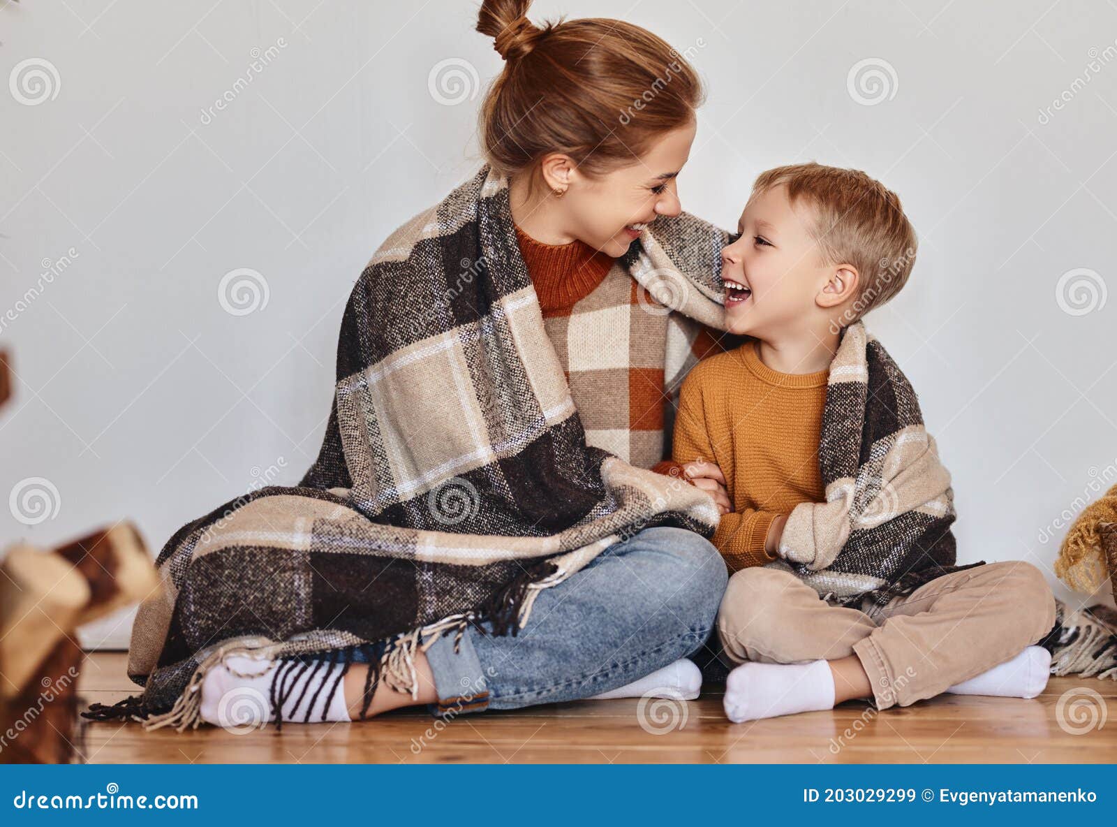 happy family mother and loving son hug and laugh wrapped in a warm blanket on  evening at home