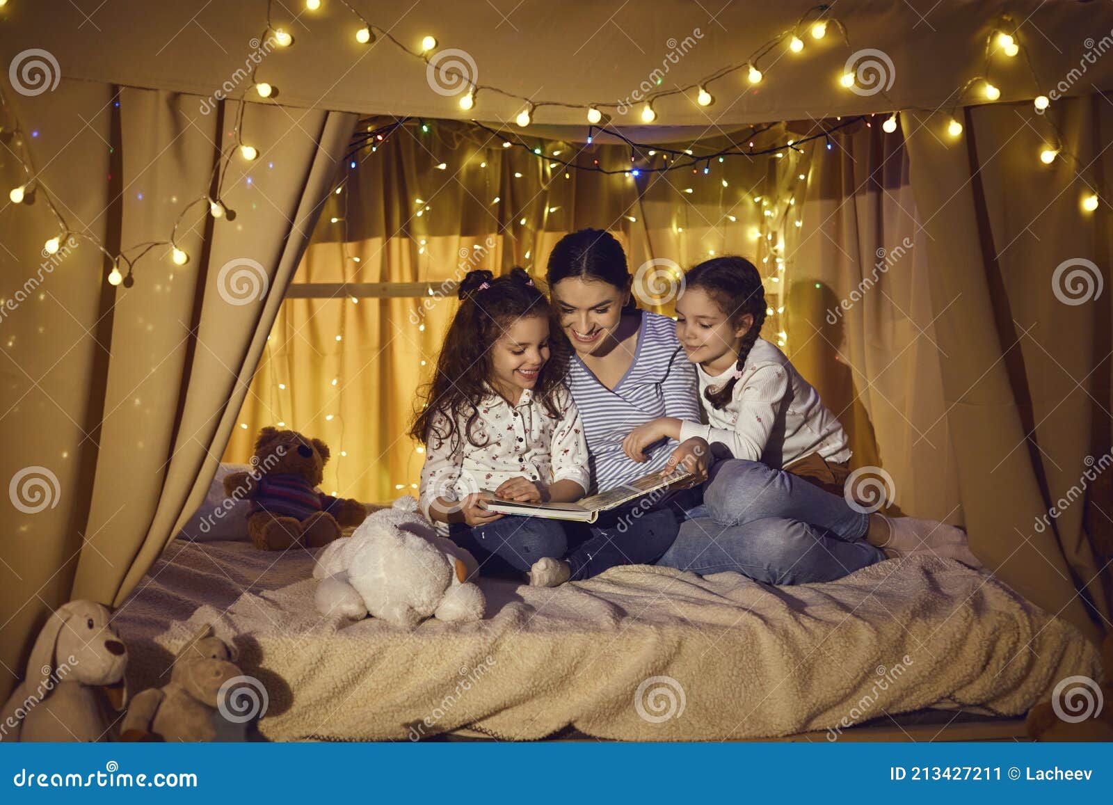 happy mother and children sitting in playroom tent and reading book of fairy tales
