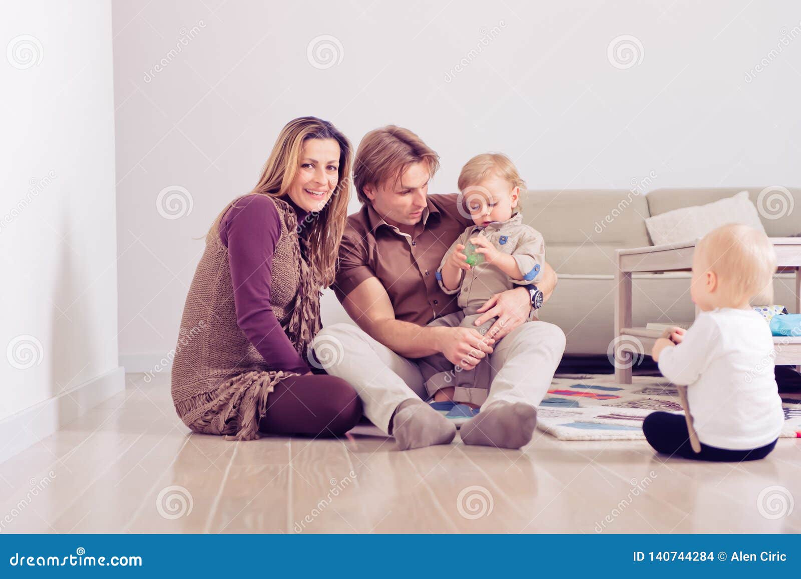 Happy Family Sitting On Floor With Their Little Babies Family