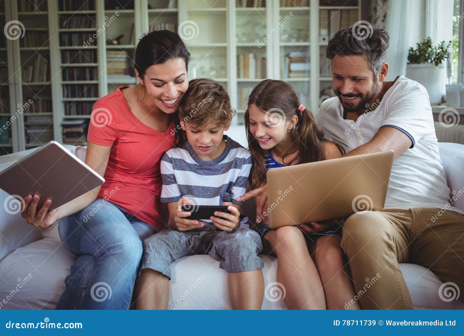 Happy family sitting on sofa and using laptop, mobile phone and digital tablet