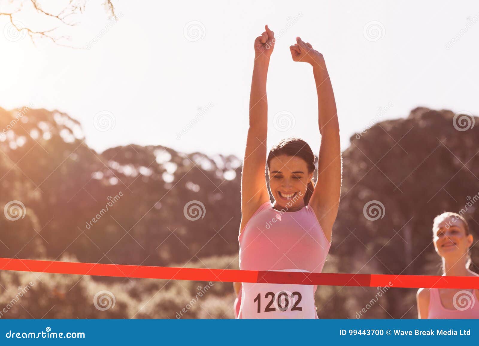 happy female athlete with arms raised crossing finish line
