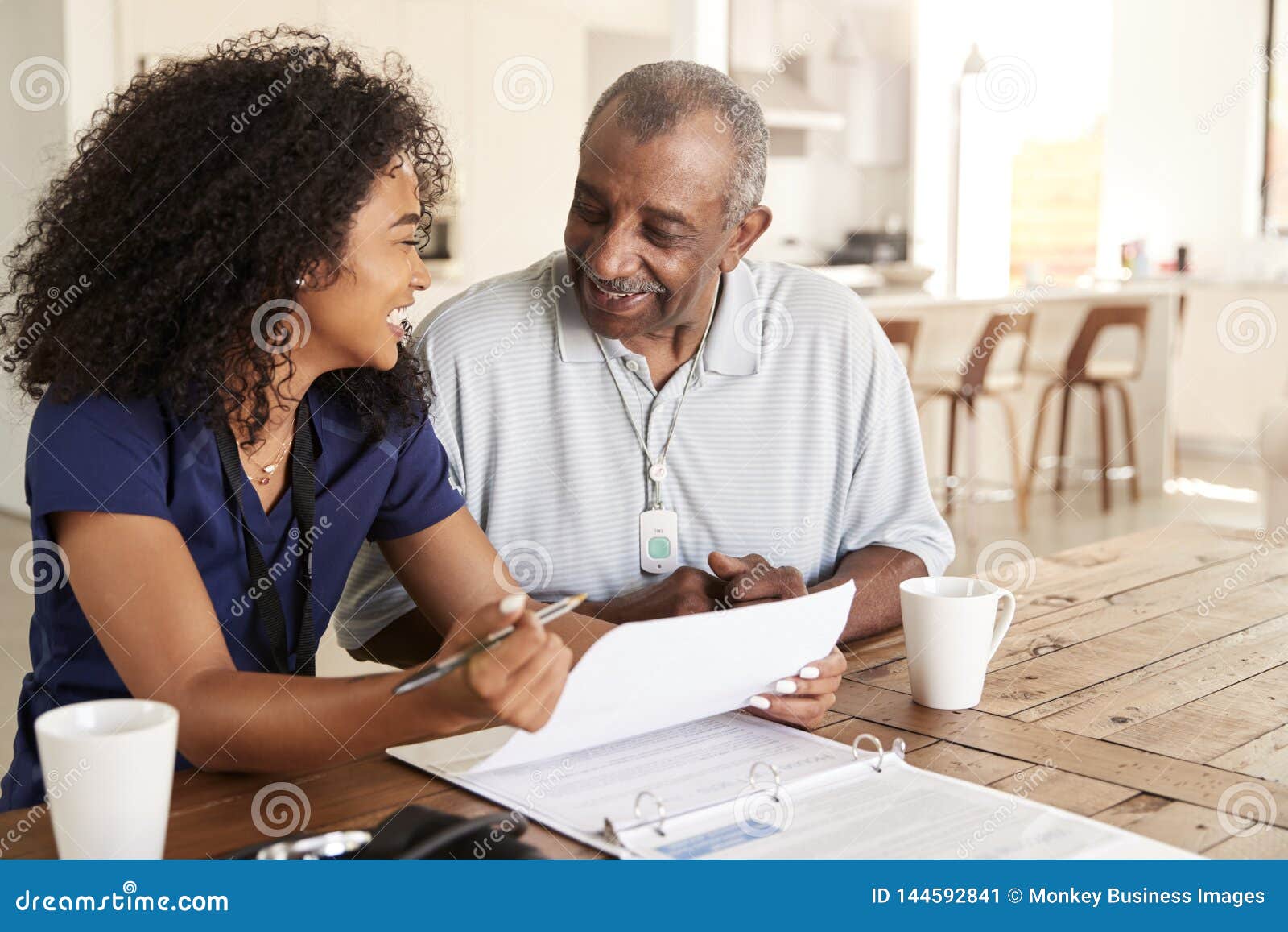 happy female healthcare worker sitting at table smiling with a senior man during a home health visit