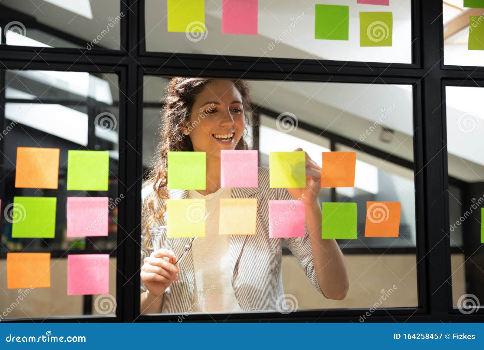 happy female scrum master writing tasks on sticky paper notes.