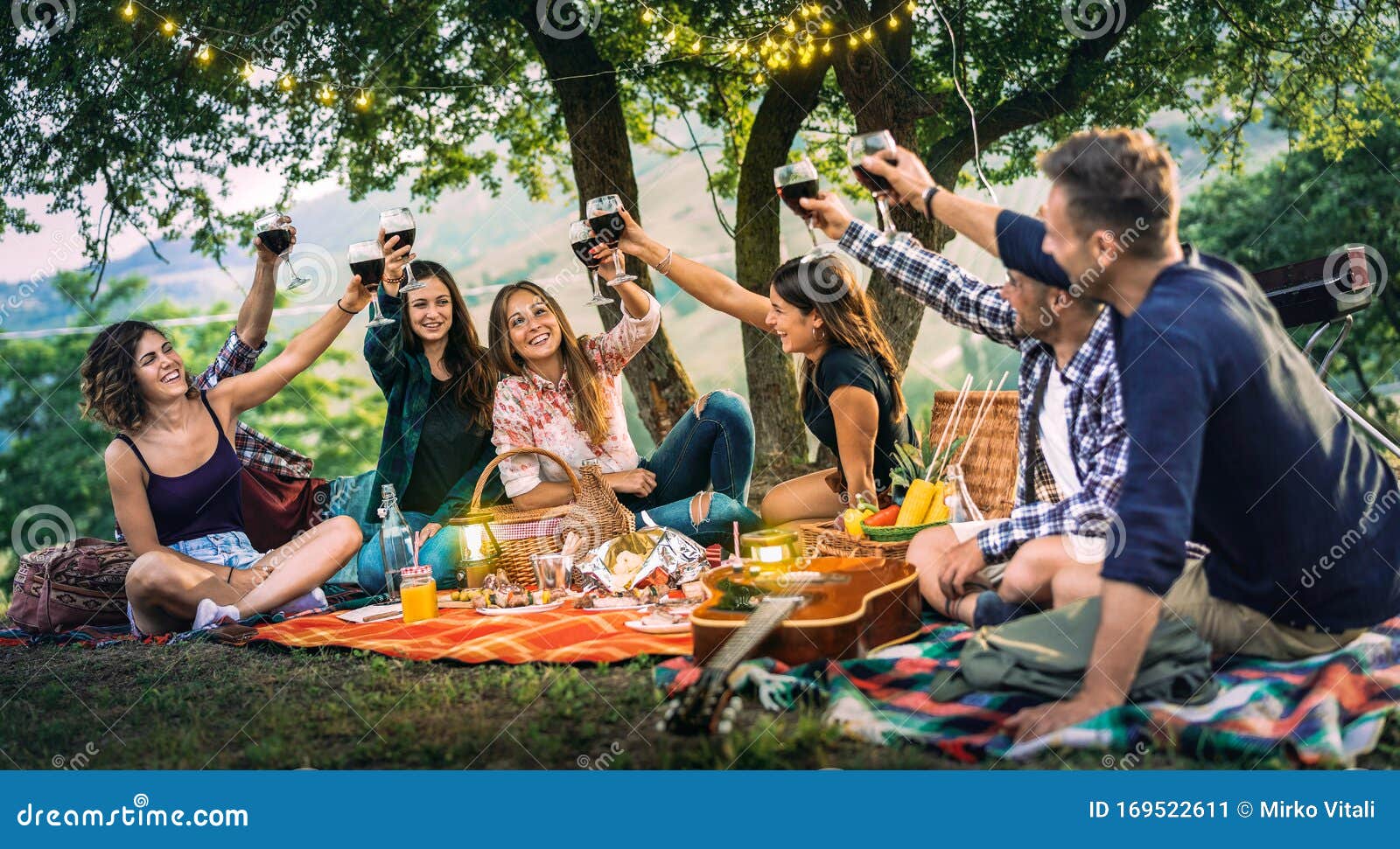 happy friends having fun at vineyard on sunset - young people millenial toasting at open air picnic under string light