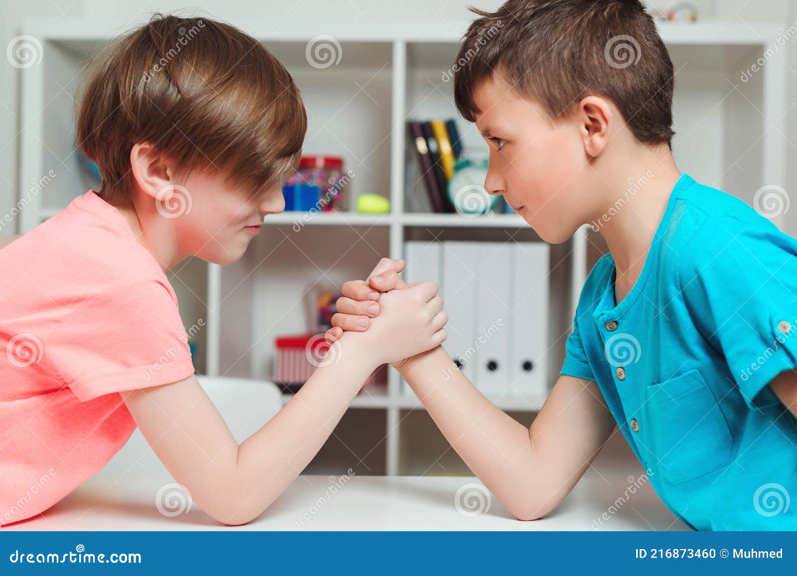 happy friends playing arm wrestle looking at each other. cute brothers spending time together at home