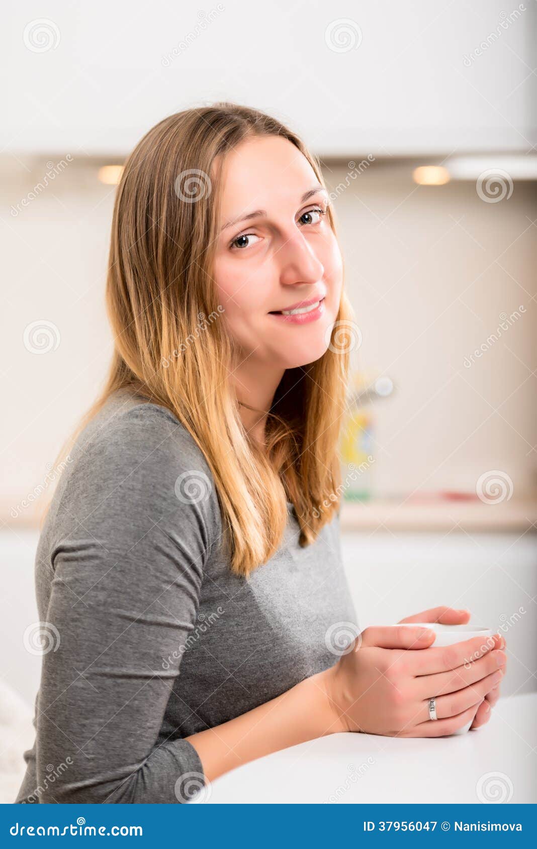 Happy girl in grey holding mug vertical. Happy girl in grey holding mug and looking at camera with smile