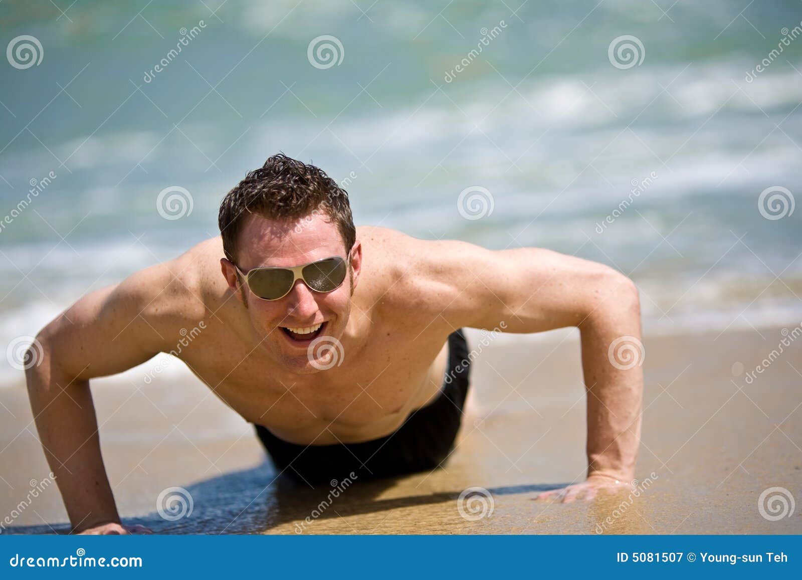 Happy guys getting up from the. Young Caucasian hunk smiling and getting up from the sandy beach