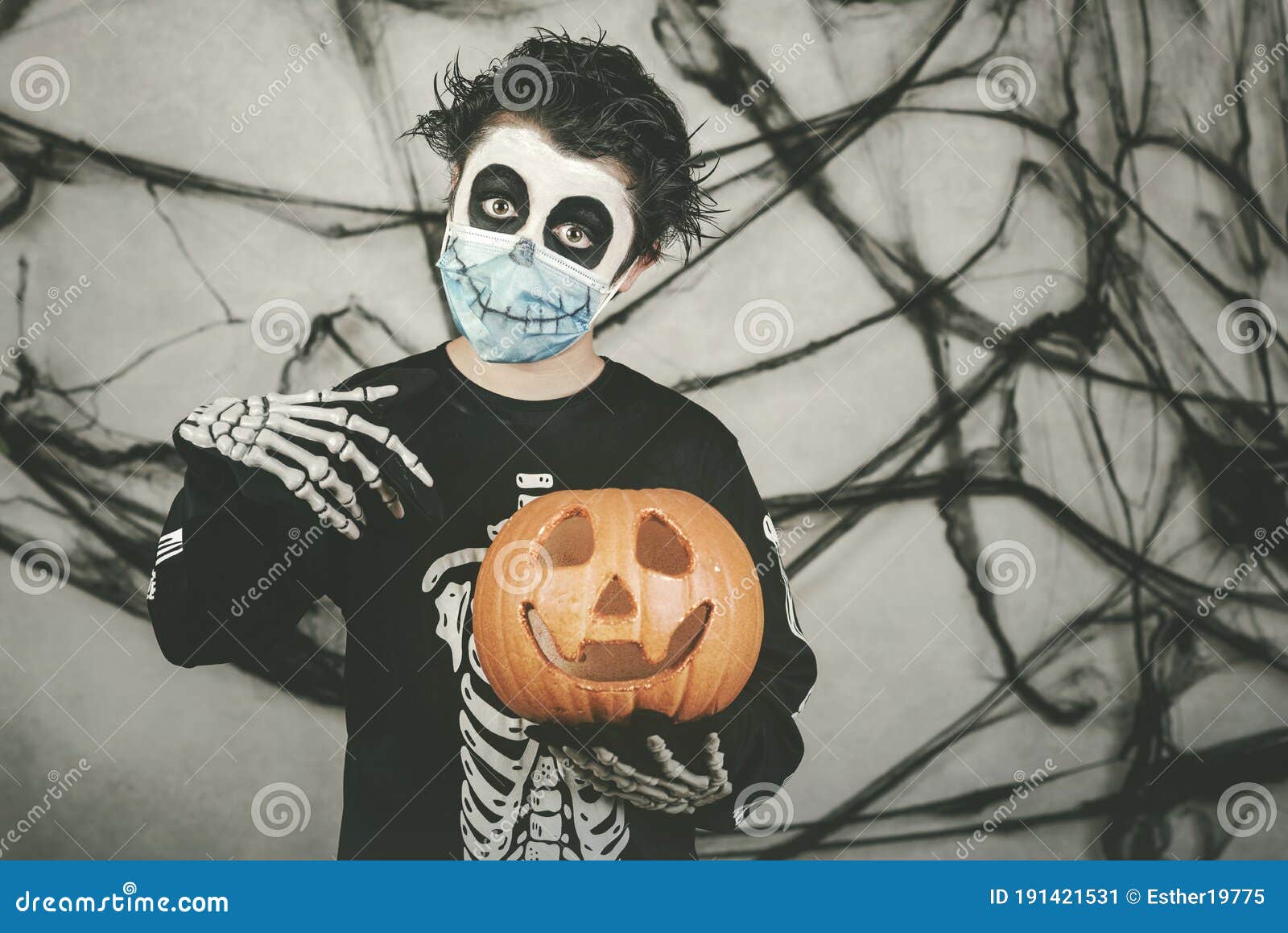 happy halloween.kid wearing medical mask in a skeleton costume with halloween pumpkin